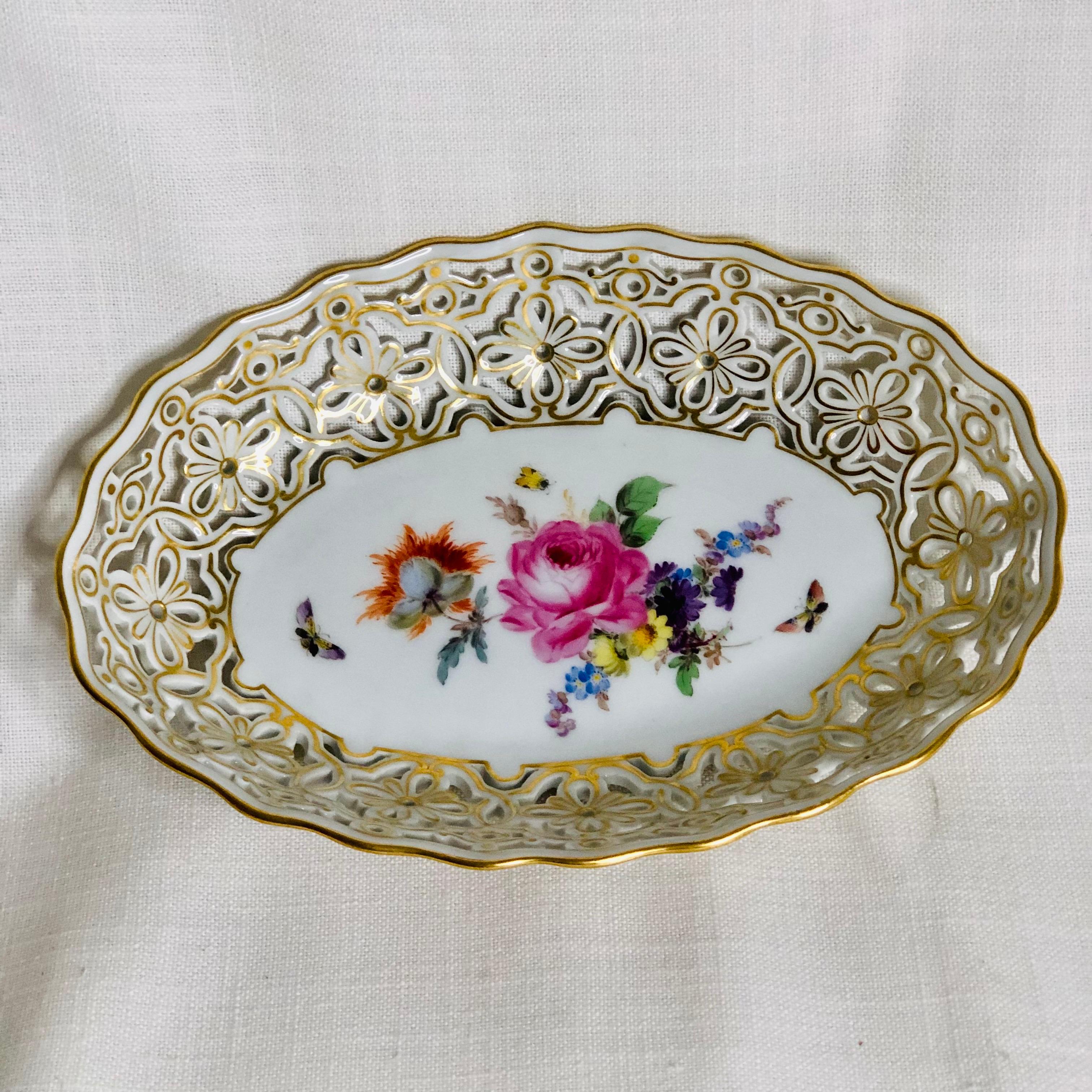 This is a beautiful oval Meissen reticulated bowl hand painted with a central painting of a flower bouquet and accents of butterflies and insects. The wonderful flowered shaped reticulation on this bowl is surrounded by a gold border on its top and