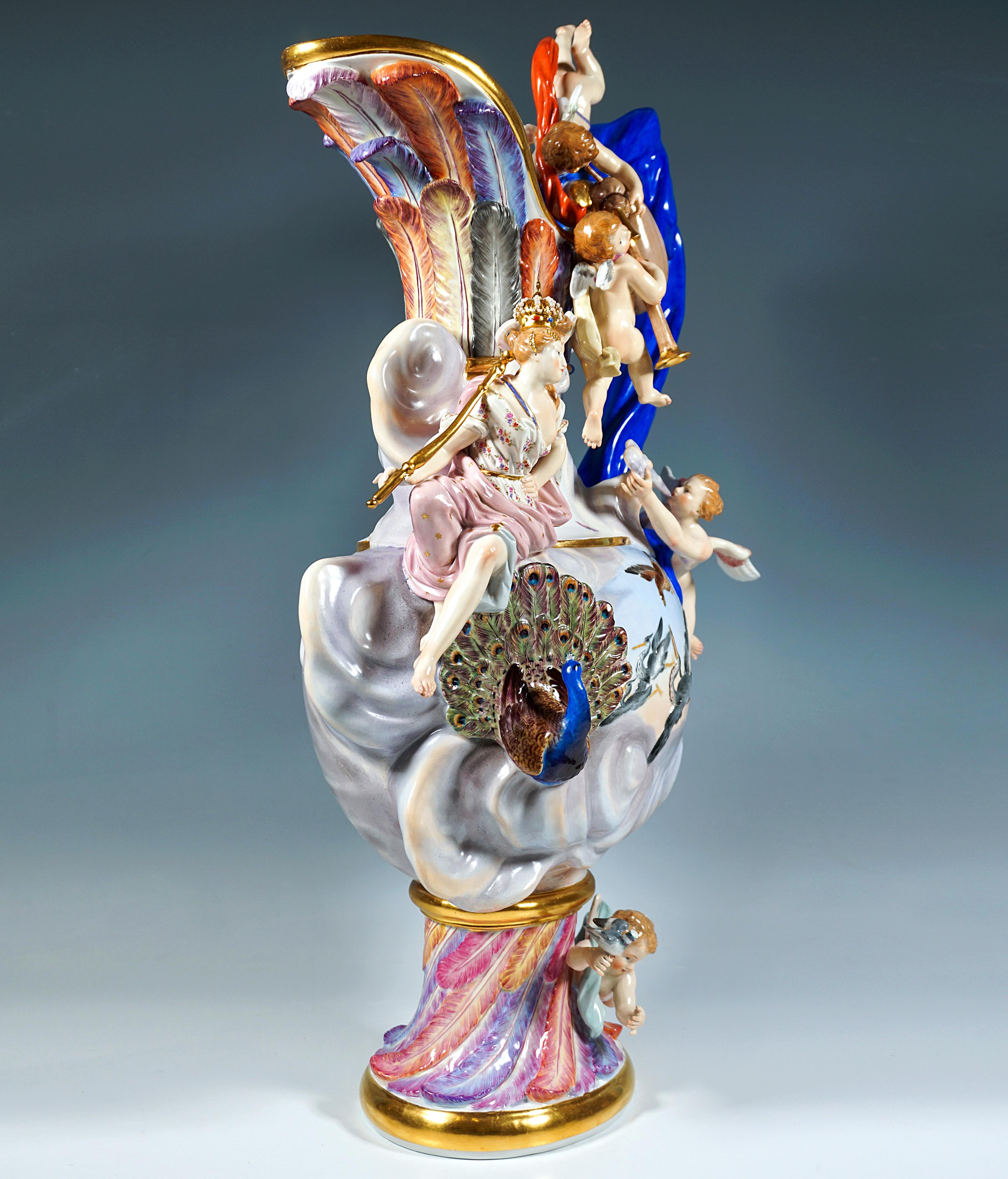 Large, ornate vase in the shape of a jug with highly embossed, partially three-dimensional decoration: on a separate oval base with colourful, diagonal feather trim, bulbous body nestled in clouds at the bottom with a separate, indented neck