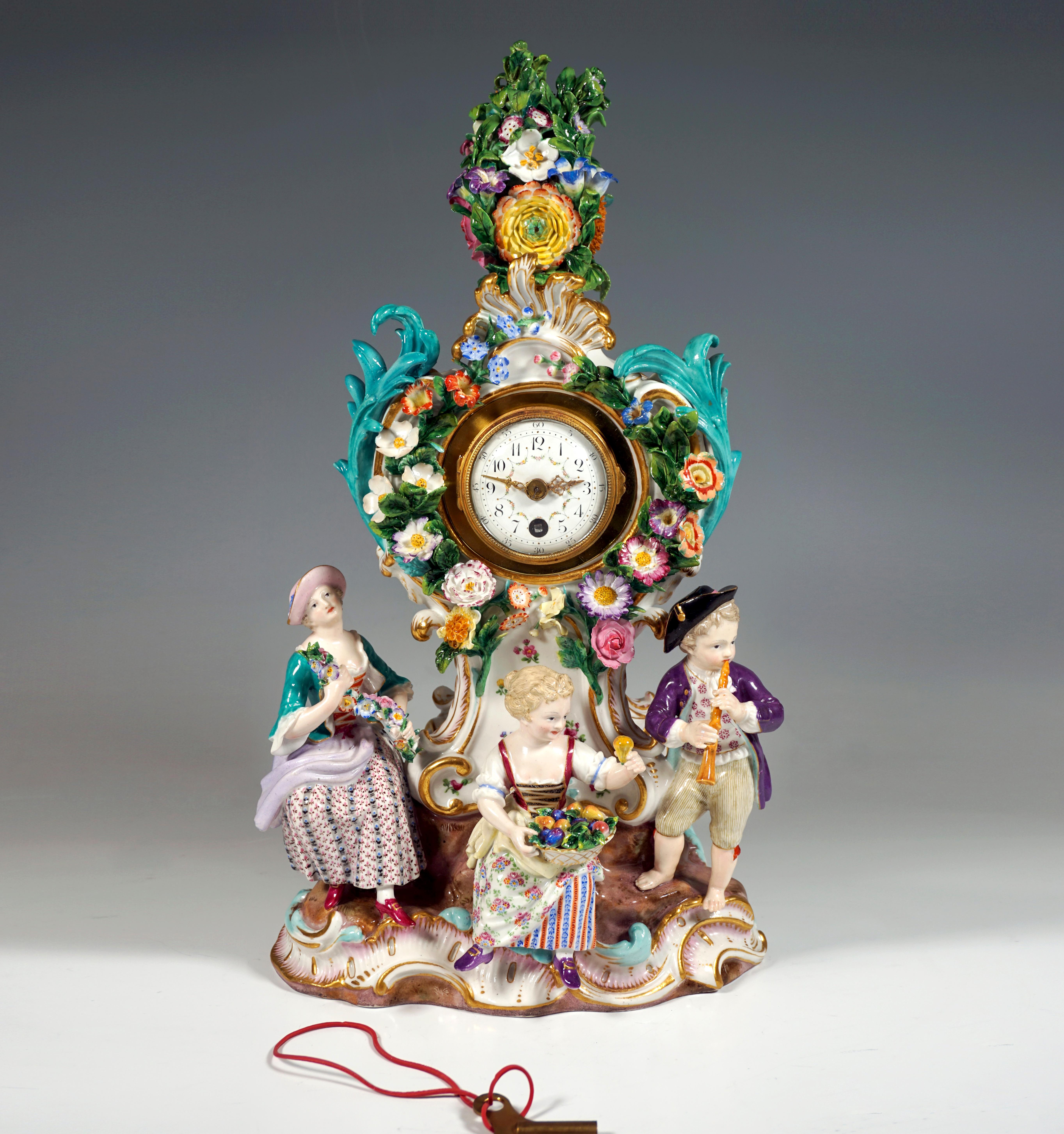 The clock was designed by Leuteritz in the Rococo style using old moulds: 
The clock case rises on a rock base with gold-heightened rocailles, richly decorated with delicate, plastically formed flowers, leaves and rocailles playing around the dial.