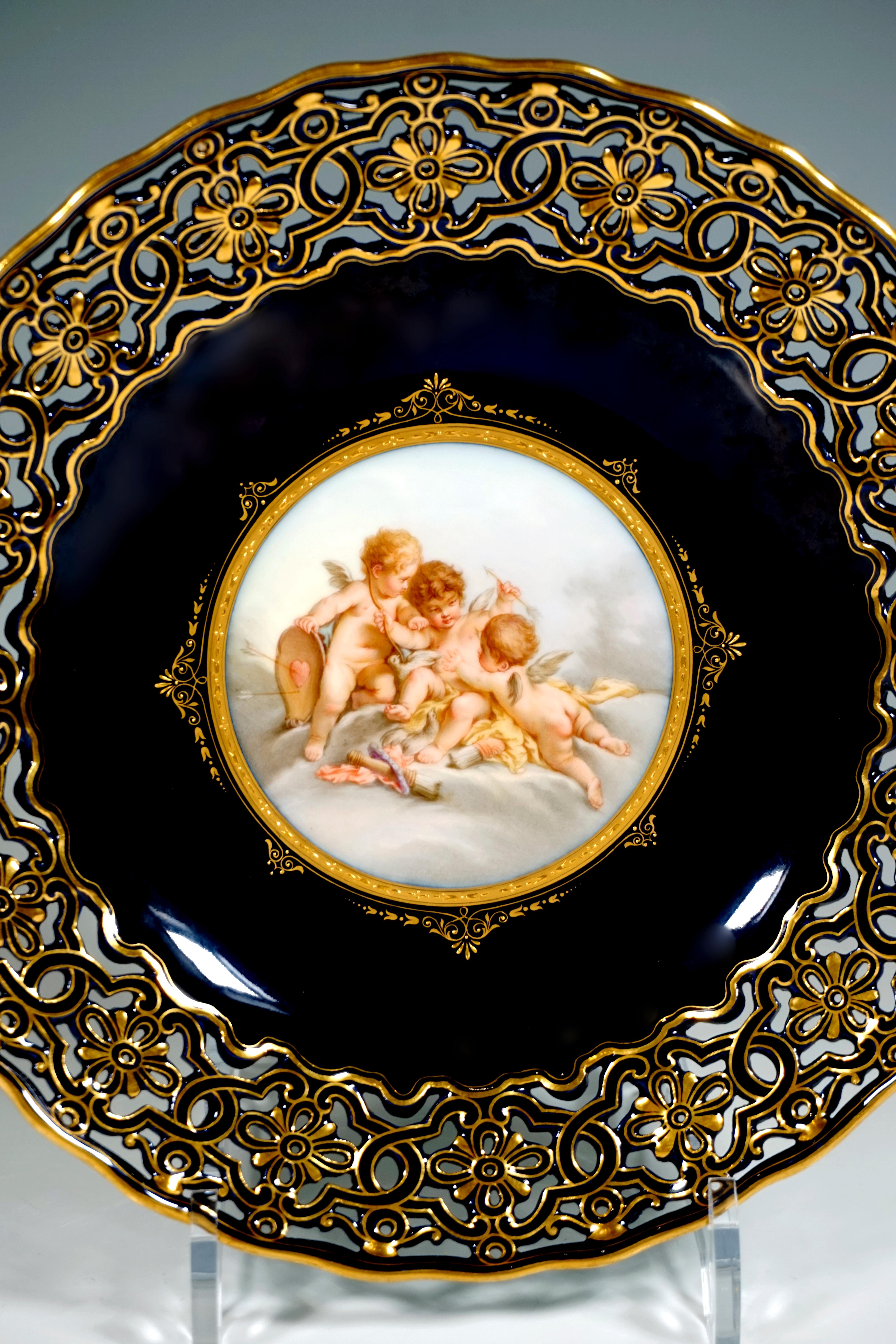 Elegant splendour plate with cobalt blue background painting, in the center a round medallion with the finest, polychrome painting depicting three cupids wrestling in a cloudy landscape, matt gold rim with impasto decoration in shiny gold,