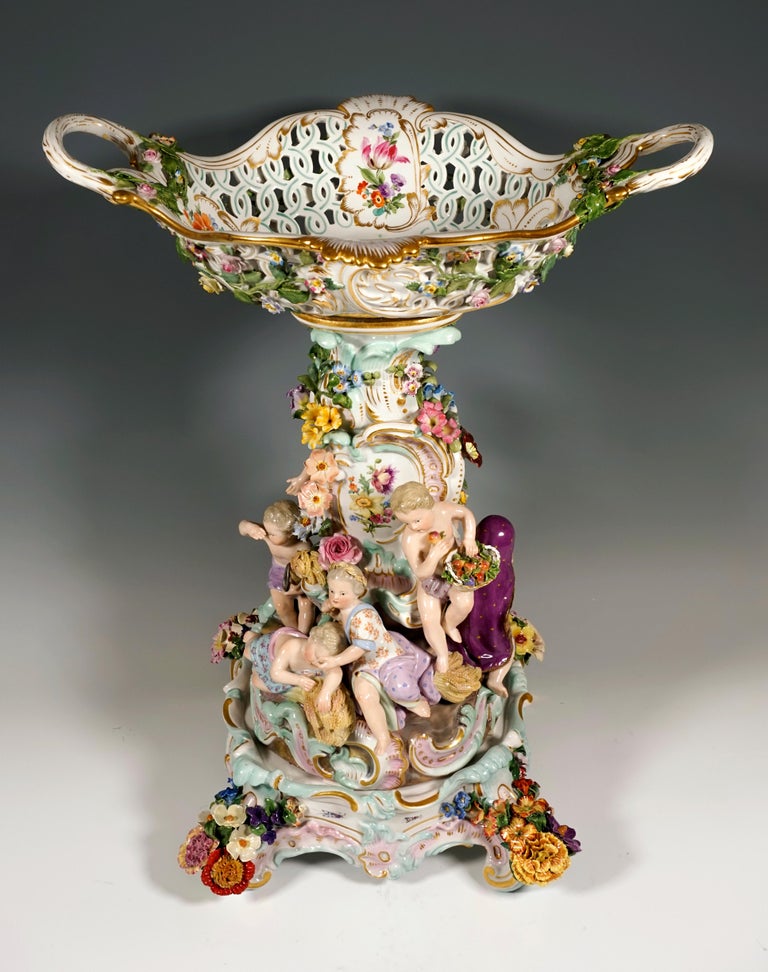 The centerpiece was designed by Leuteritz using old moulds in the Rococo style: a curved column rises on a rock base with gold rocailles, richly decorated with delicate, three-dimensional flowers, leaves and rocailles. Below are eight cupids sitting