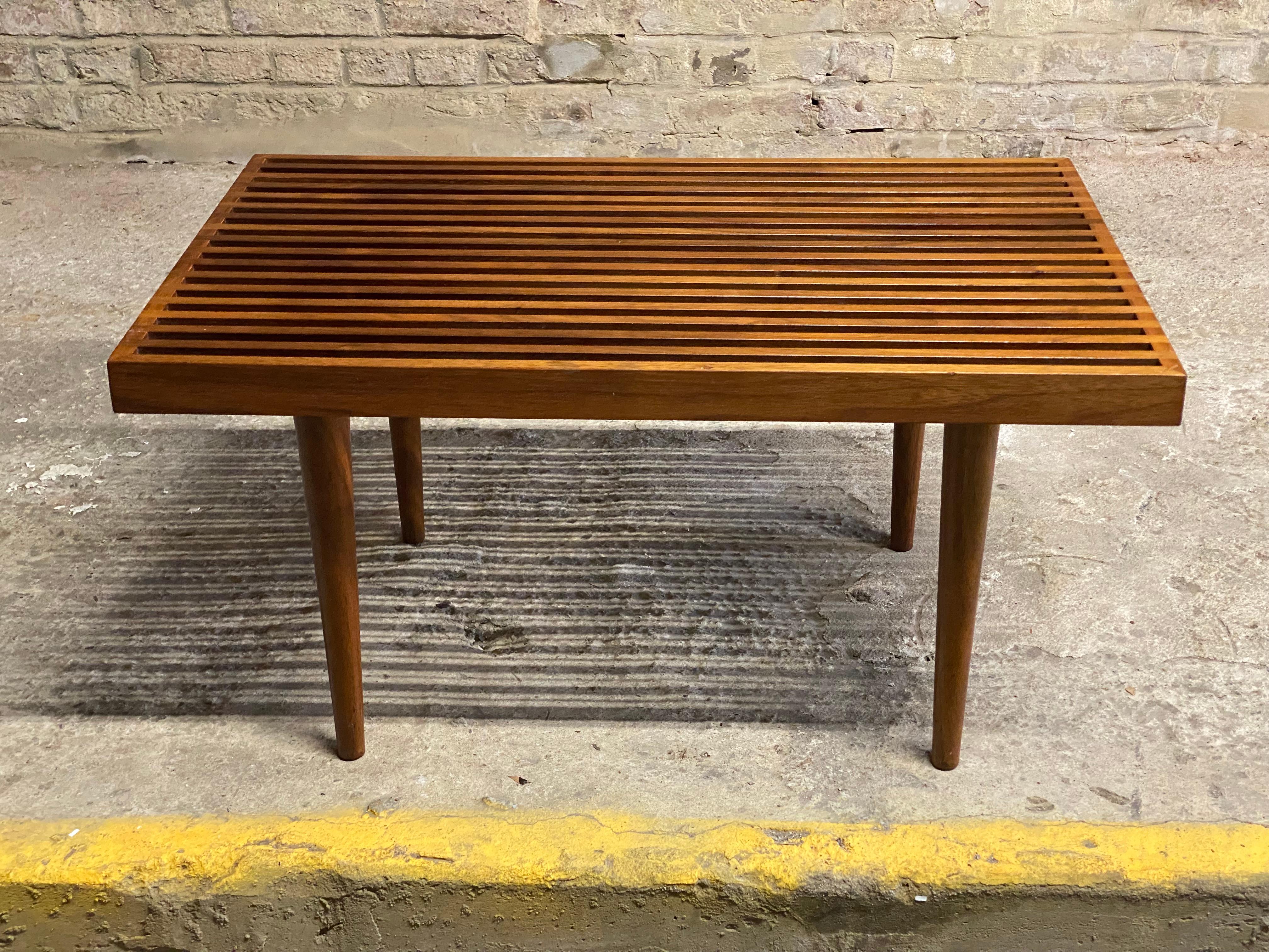 A Mel Smilow (1922-2002) designed solid walnut slat table. Wonderful oiled walnut featuring that signature splined corners, cross cut color contrast sides and removable tapered legs. Flat pack design. These are great accent tables or small benches