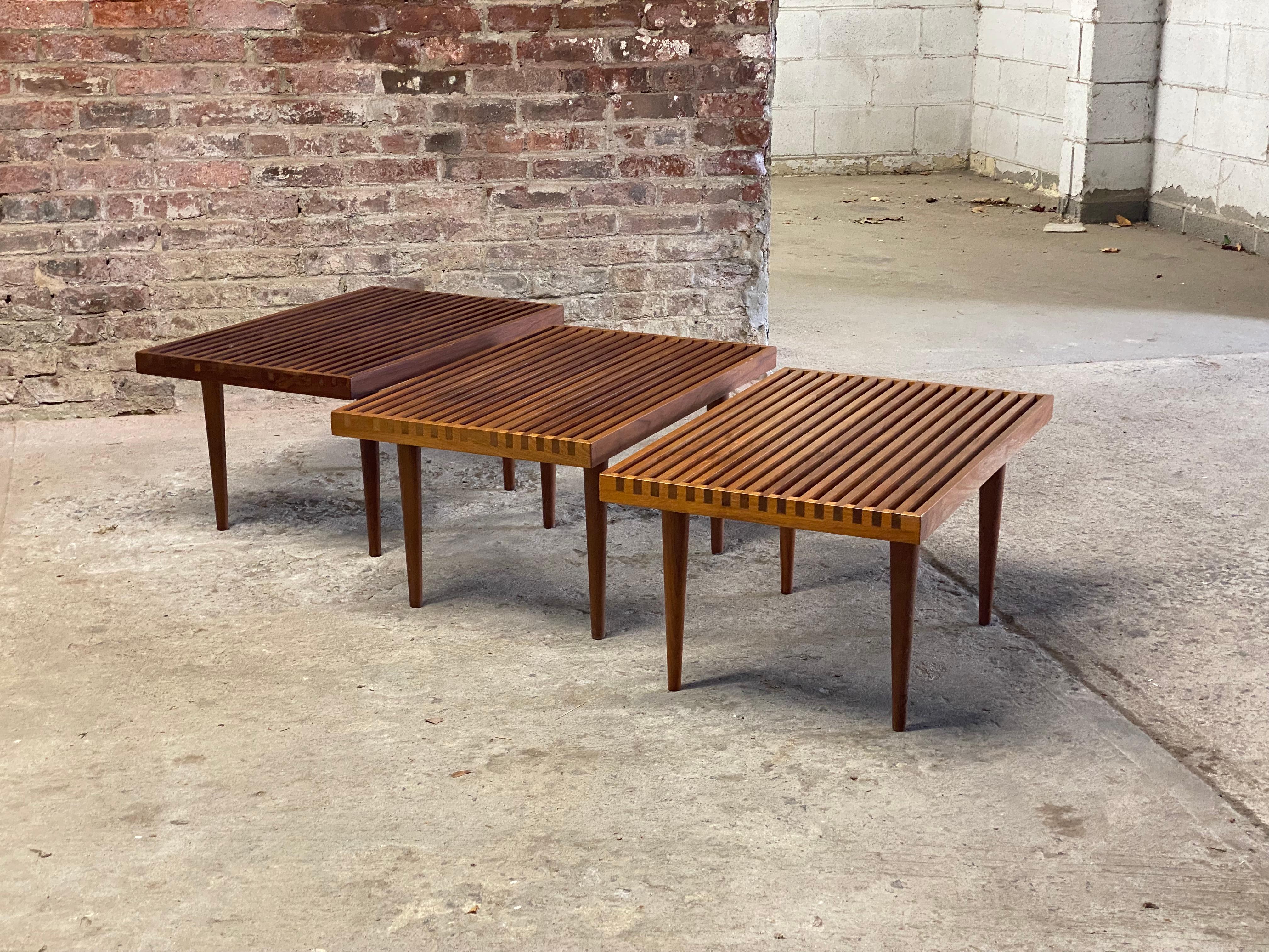 A fine set of three Mel Smilow (1922-2002) designed solid walnut slat tables. Wonderful oiled walnut featuring that signature splined corners, cross cut color contrast sides and removable tapered legs. Flat pack design. These are great accent tables