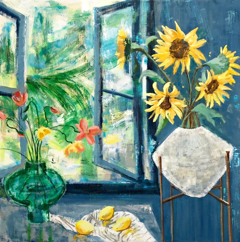 In this bright and inviting interior scene, an arrangement of cheerful yellow sunflowers in a planter on a stand sit beside a table with three yellow lemons and a bouquet of coral and yellow flowers in a vase over a white striped tablecloth. The