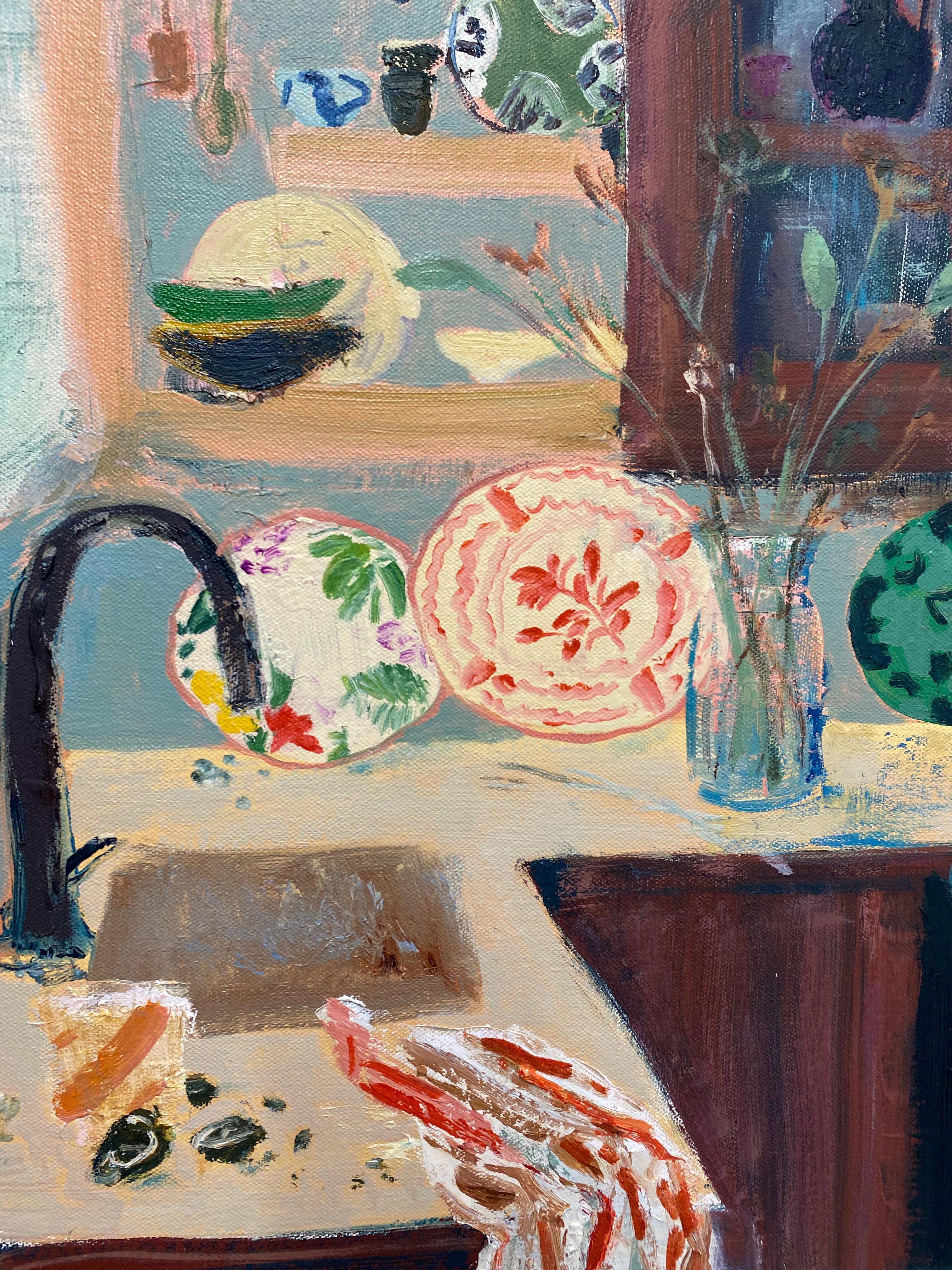 Scène d'intérieur lumineuse et accueillante avec des assiettes en porcelaine à motifs colorés posées à côté d'une composition florale avec des fleurs vertes dans un vase sur le comptoir de la cuisine et une théière rouge cramoisi. Des tasses à thé