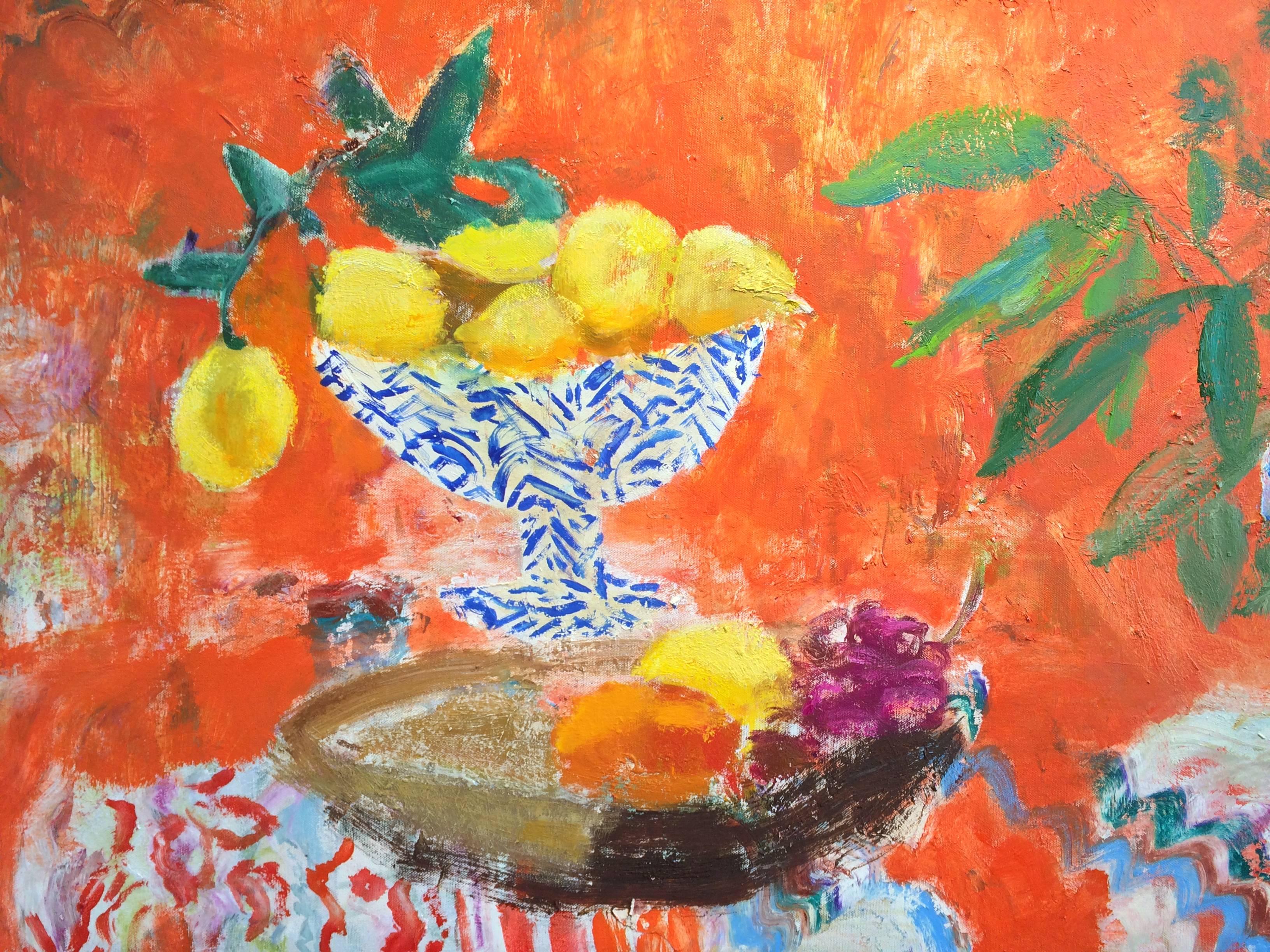 Una scena d'interni luminosa e invitante con una composizione di limoni in una fruttiera dipinta di blu e bianco accanto a una pianta verde e frondosa in un vaso blu e bianco su una tovaglia a righe, colorata e a fantasia. Una fruttiera marrone poco