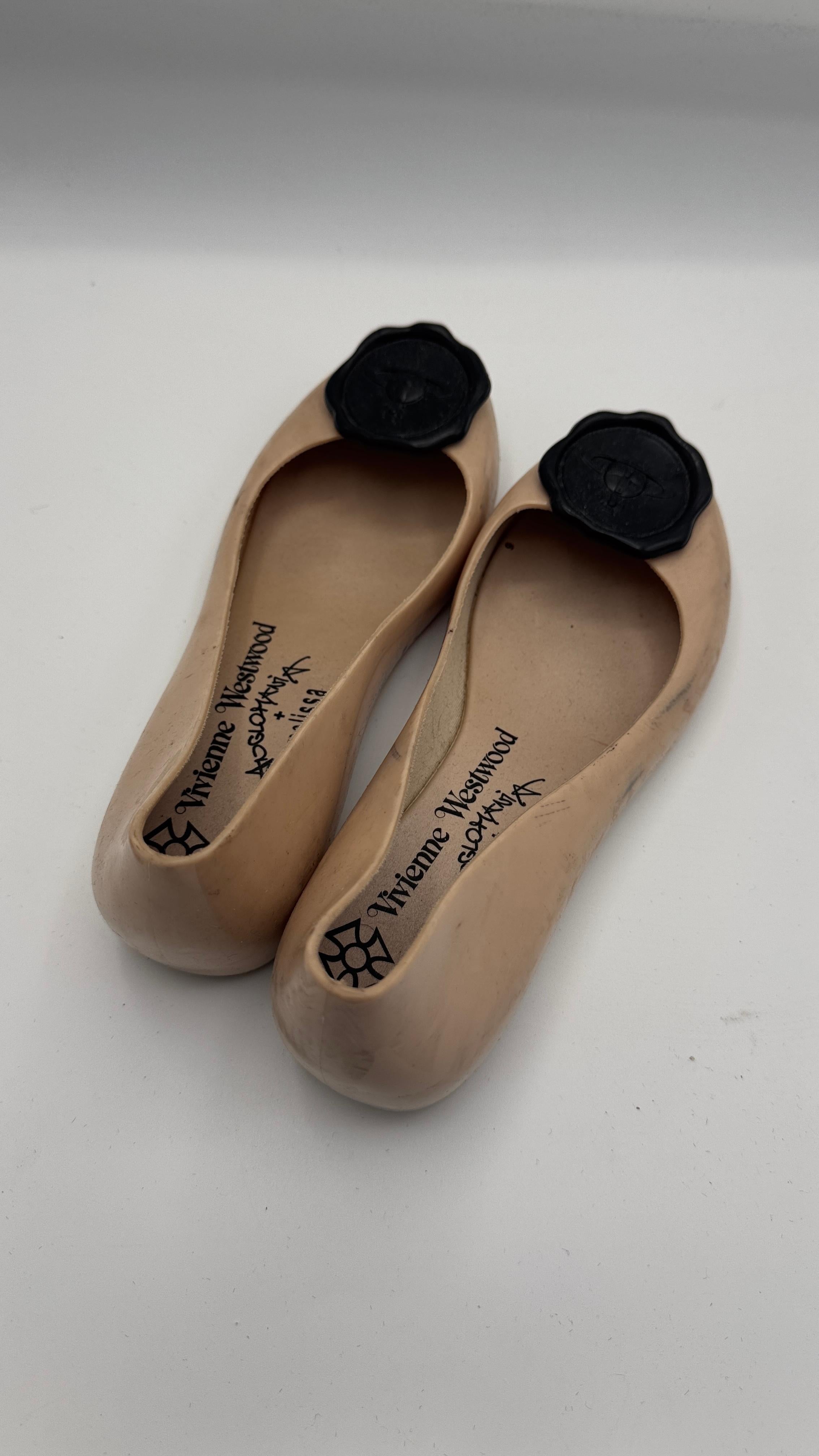 Icónico par de bailarinas Melissa x Vivienne Westwood Anglomania en PVC perfumado en tono nude, con el detalle del sello de cera negro característico de la diseñadora y el logotipo Orb en la puntera. Este modelo forma parte de la primera colección