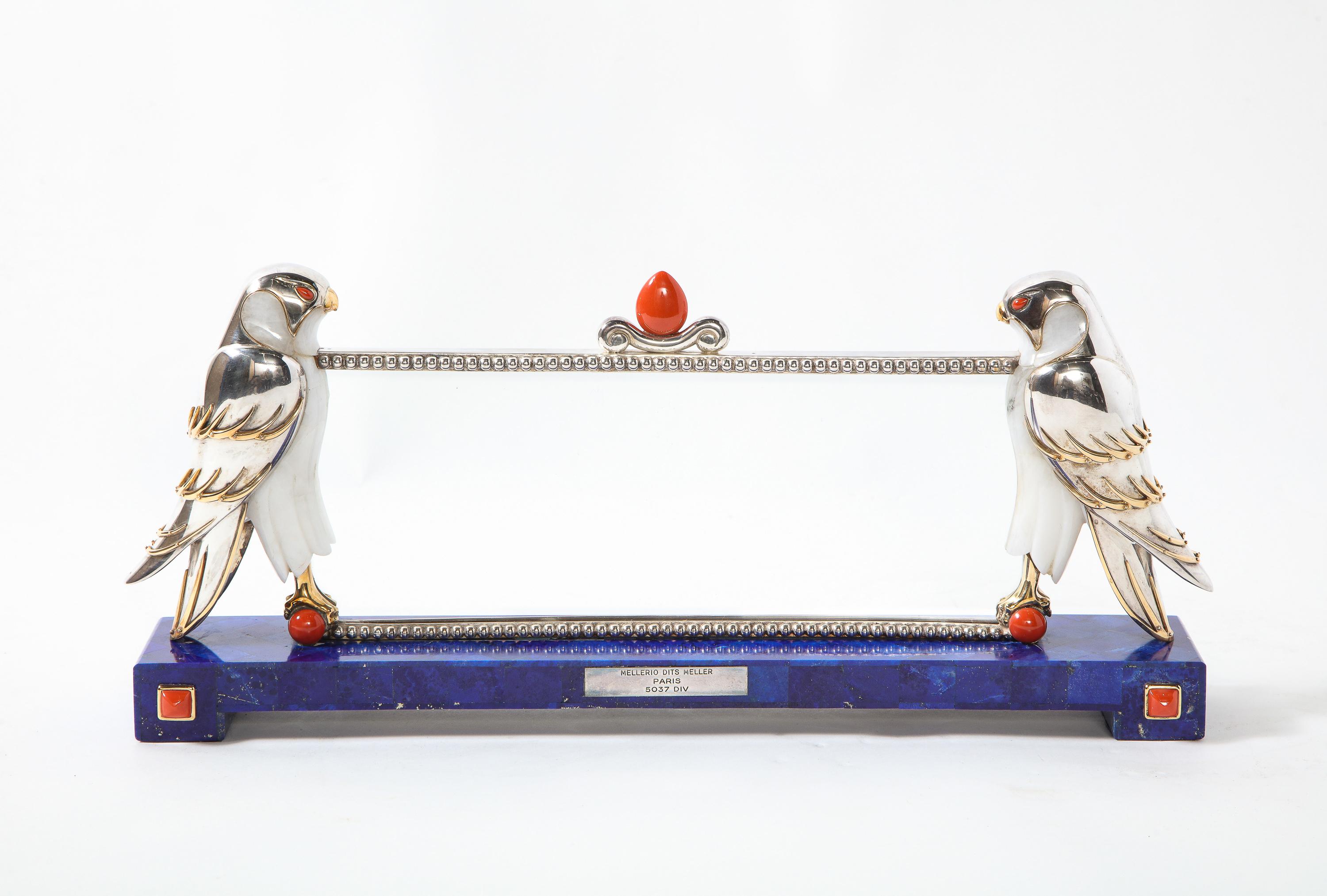 Mellerio Paris, a large silver, gold, lapis lazuli, coral, and hardstone picture photo frame with two falcons.

France, circa 2000

The frame resting on a lapis lazuli base with square coral cabochons and a plaque engraved MELLERIO DITS MELLER /