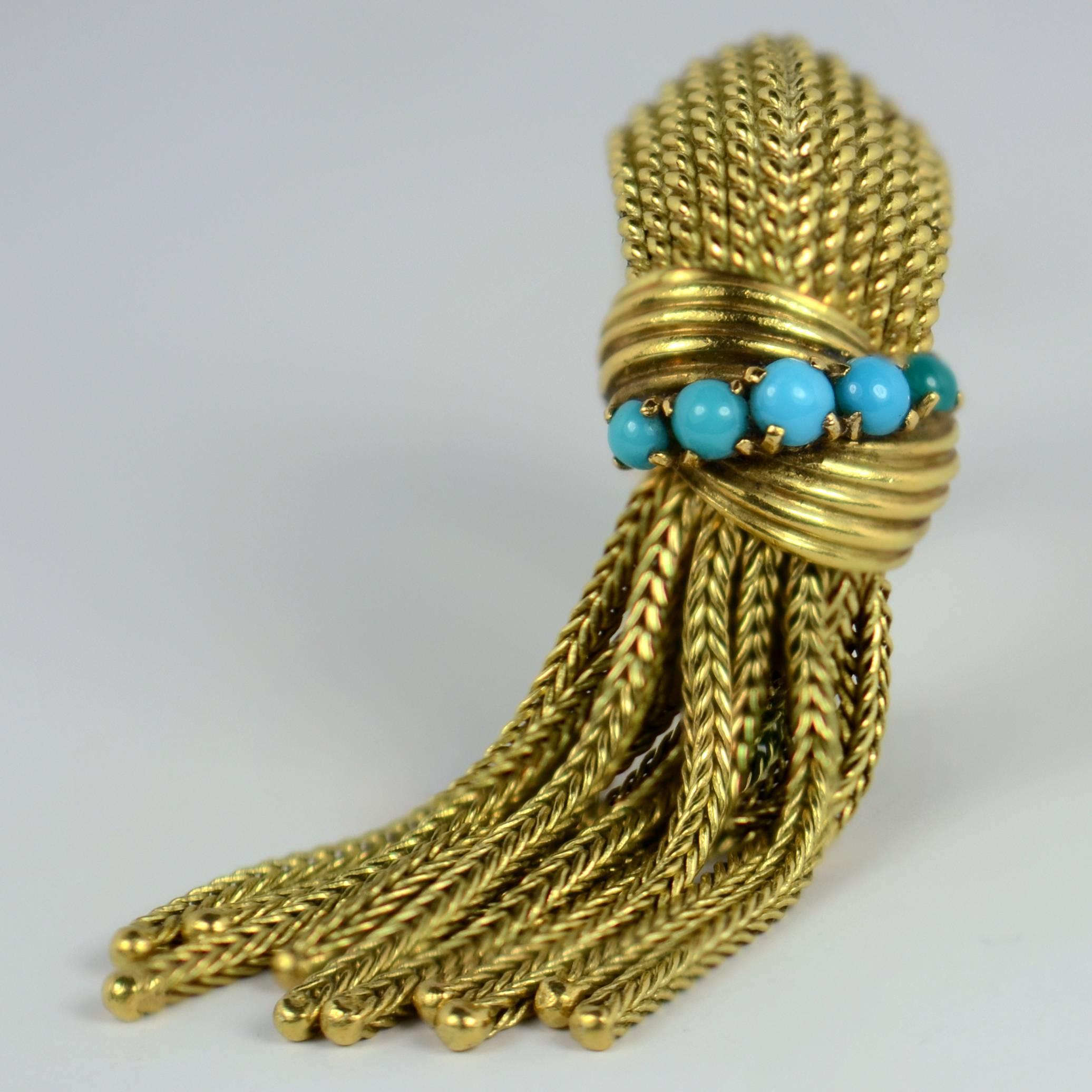 A chic pinky ring signed Mellerio in 18 karat gold set with five turquoise above a fringe tassel.  The ridged dome ring is designed as twists of gold to give a braided effect, with a double twist of gold highlighted with turquoise cabochons above a