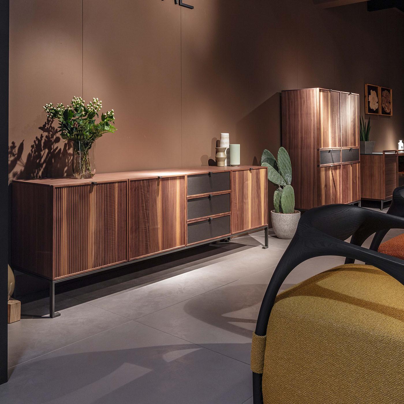 Crafted from exquisite Canaletto walnut wood and set on a sleek metal base, this storage unit exemplifies meticulous craftsmanship and elegant design. The wooden top is complemented by three fluted wood doors and three leather-fronted drawers, each