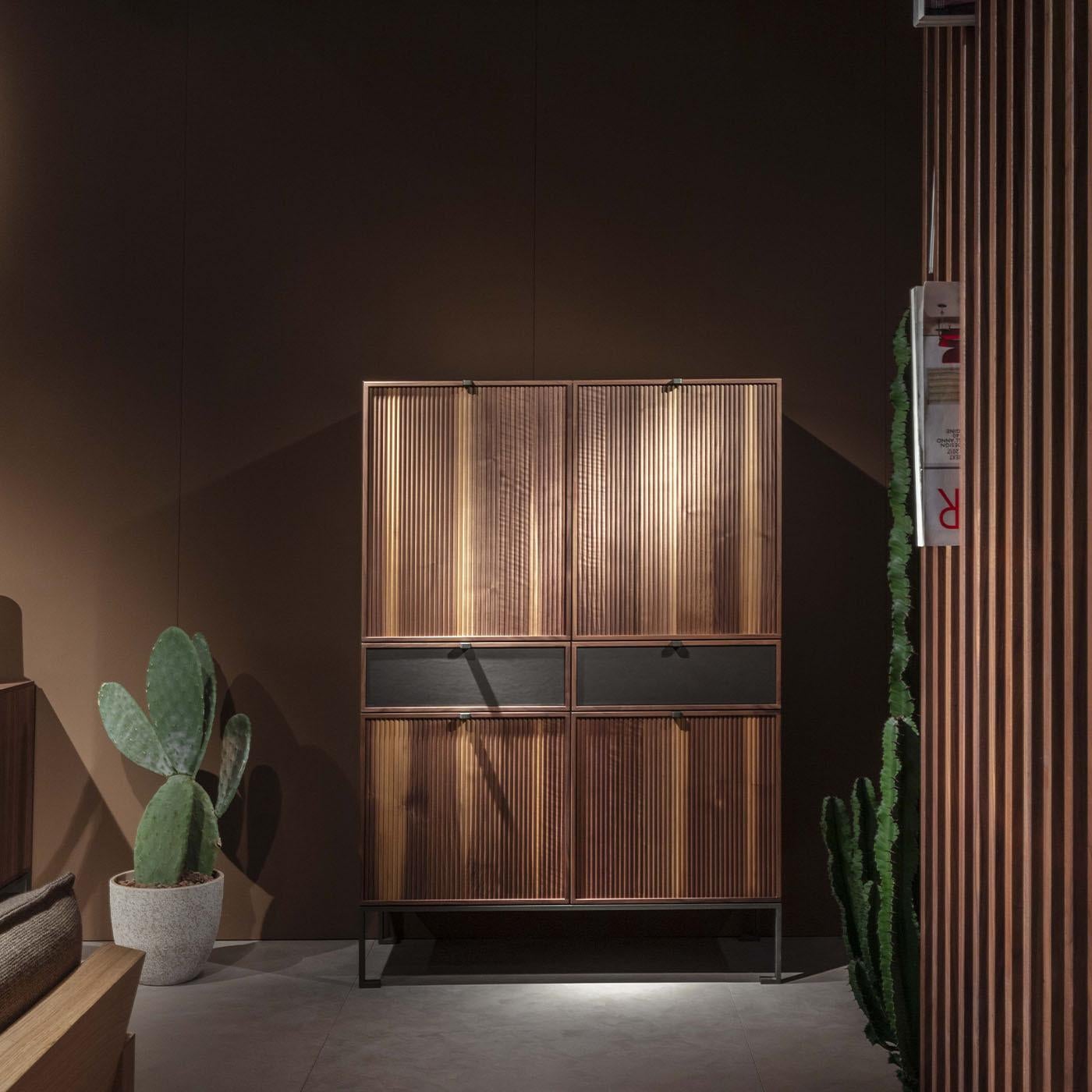 This exquisite storage unit, crafted from Canaletto walnut wood and supported by a sleek metal base, exemplifies refined craftsmanship and design. Featuring a wooden top, four fluted wood doors, and two leather-fronted drawers, every detail is