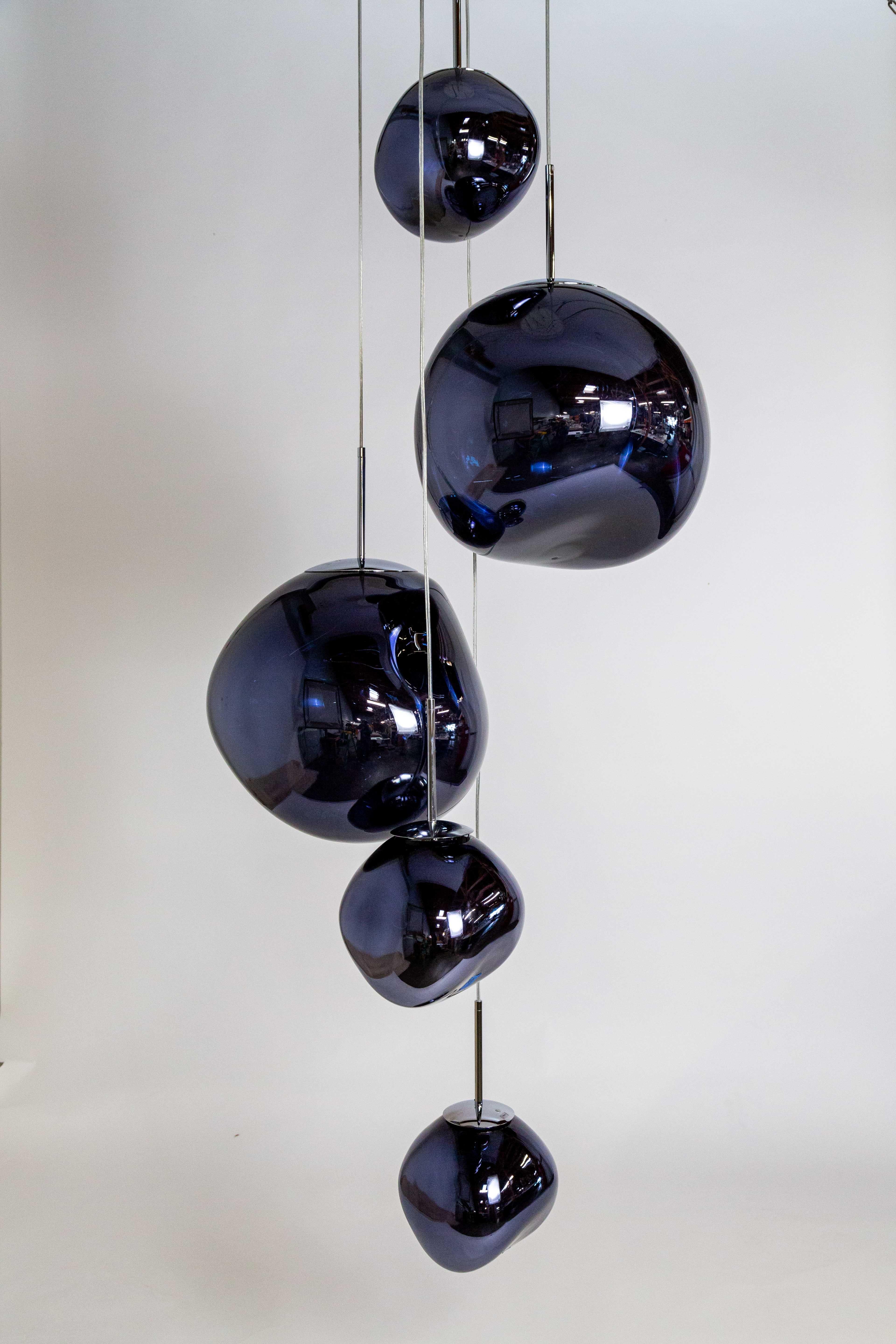 A large, cascading style chandelier featuring two spherical Melt and three Melt Mini pendant lights in a modern Smoke finish. Designed by Tom Dixon (with Maker's sticker), this ceiling light is customizable in height and ball orientation.  It