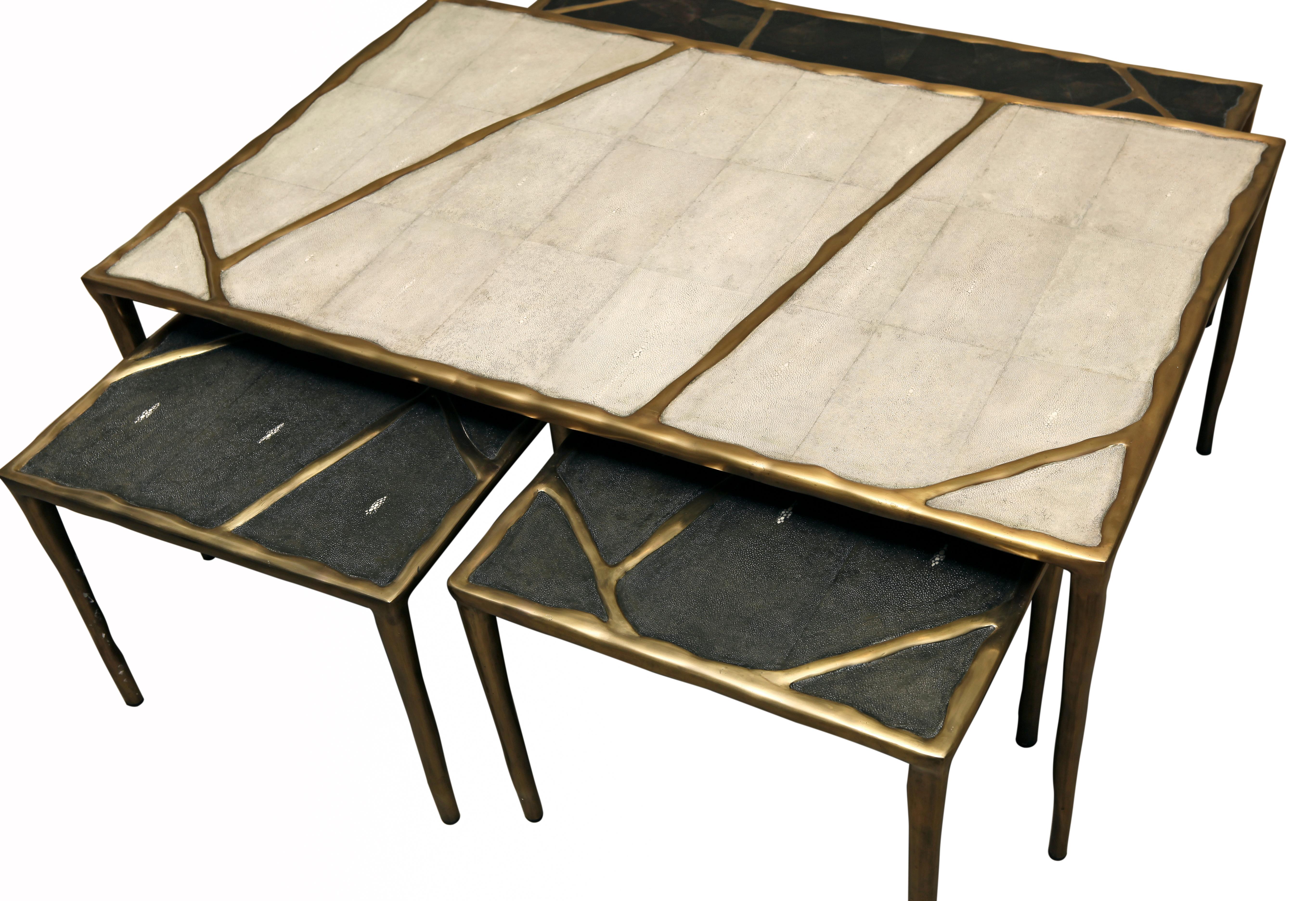 The melting nesting coffee tables are sold as a set of 4, the large is inlaid in cream shagreen, the medium in black pen shell, and the two small sizes in coal black shagreen. These pieces have a bronze-patina brass pattern that 