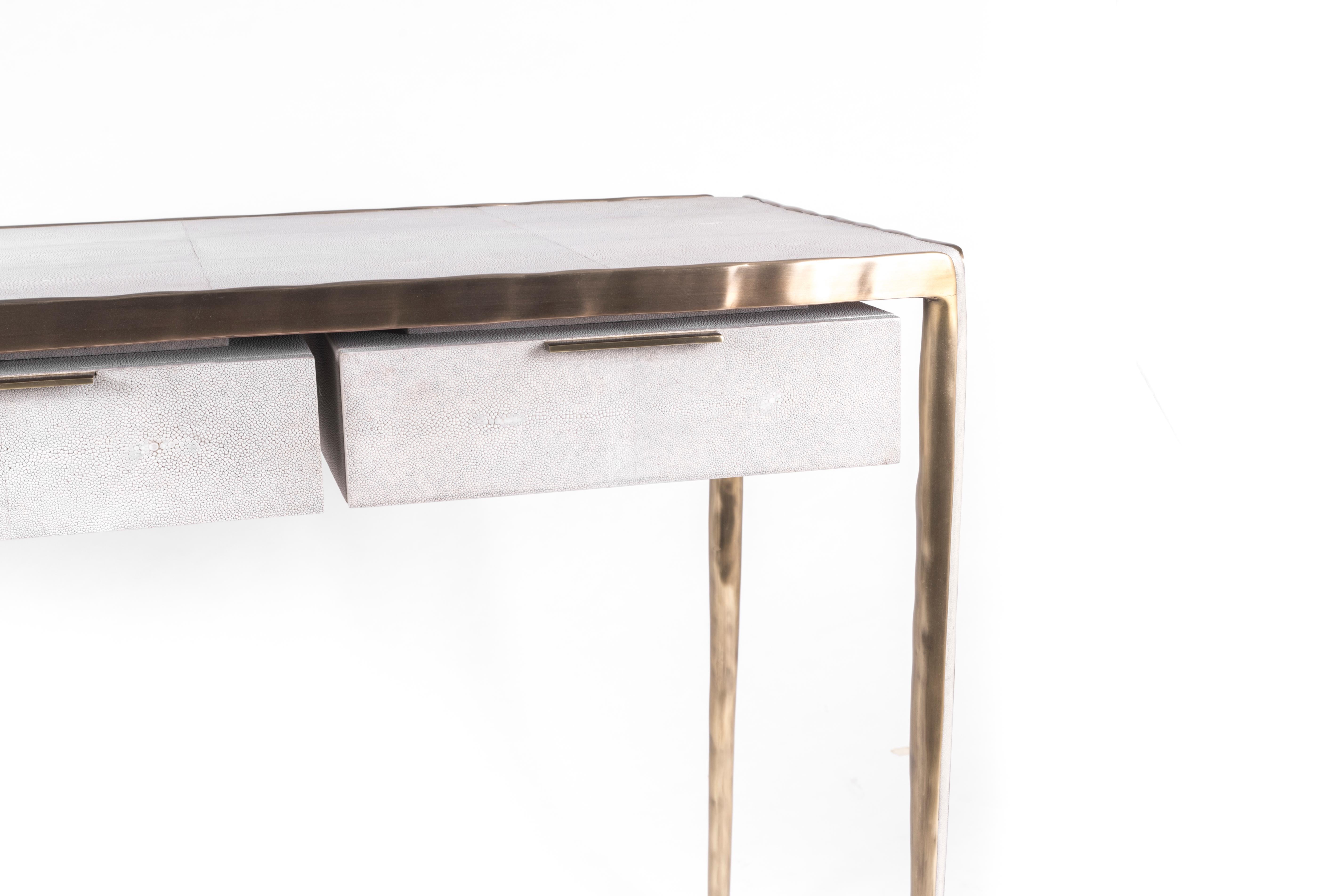 Das schlichte, aber elegante Design des Melting-Schreibtisches macht ihn zu einem anpassungsfähigen, neutralen Möbelstück. Die cremefarbene Chagrinplatte ist mit einer unregelmäßigen Oberfläche aus Bronze-Patina-Messing umrahmt, die den