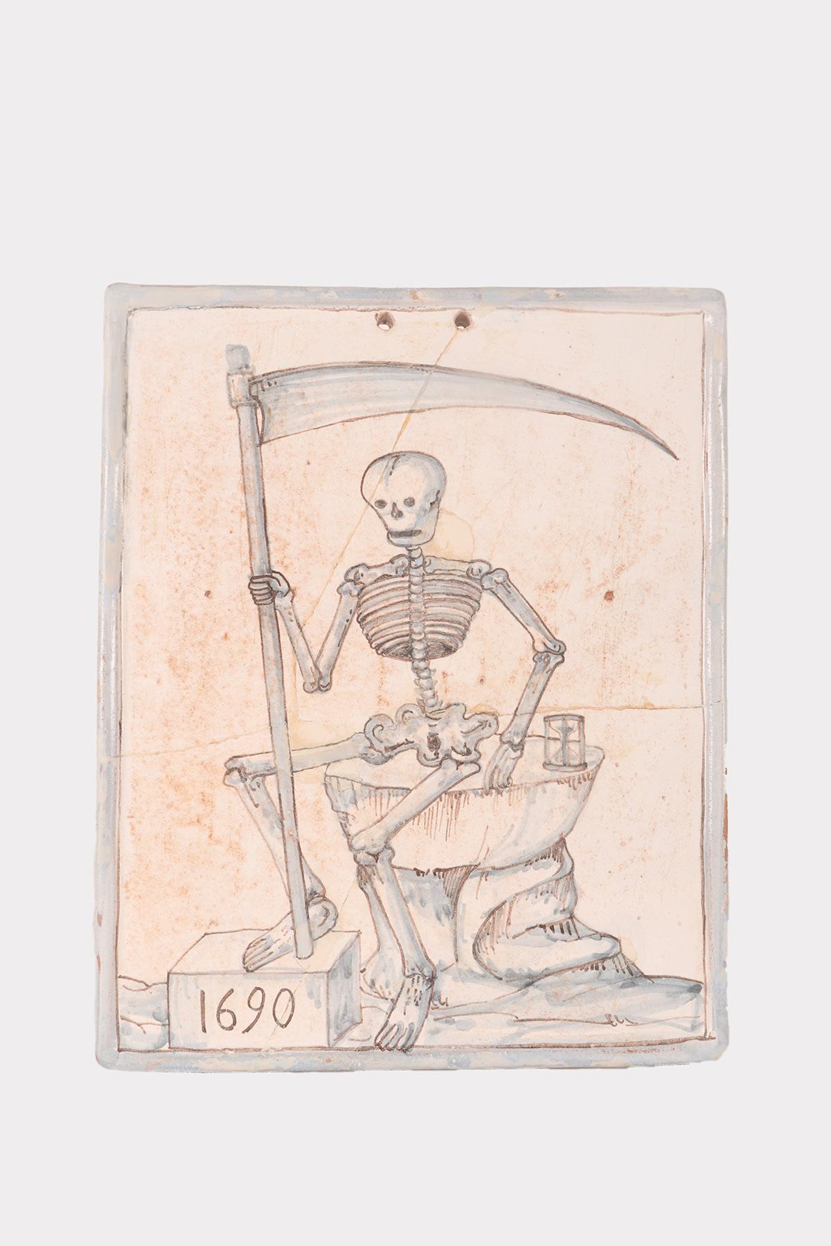 Memento Mori. A rare glazed terracotta tile with a blue painting on a white background, depicting a skeleton sitting on a rock with a scythe in his hand and an hourglass at his side. Naples, Italy 1690.