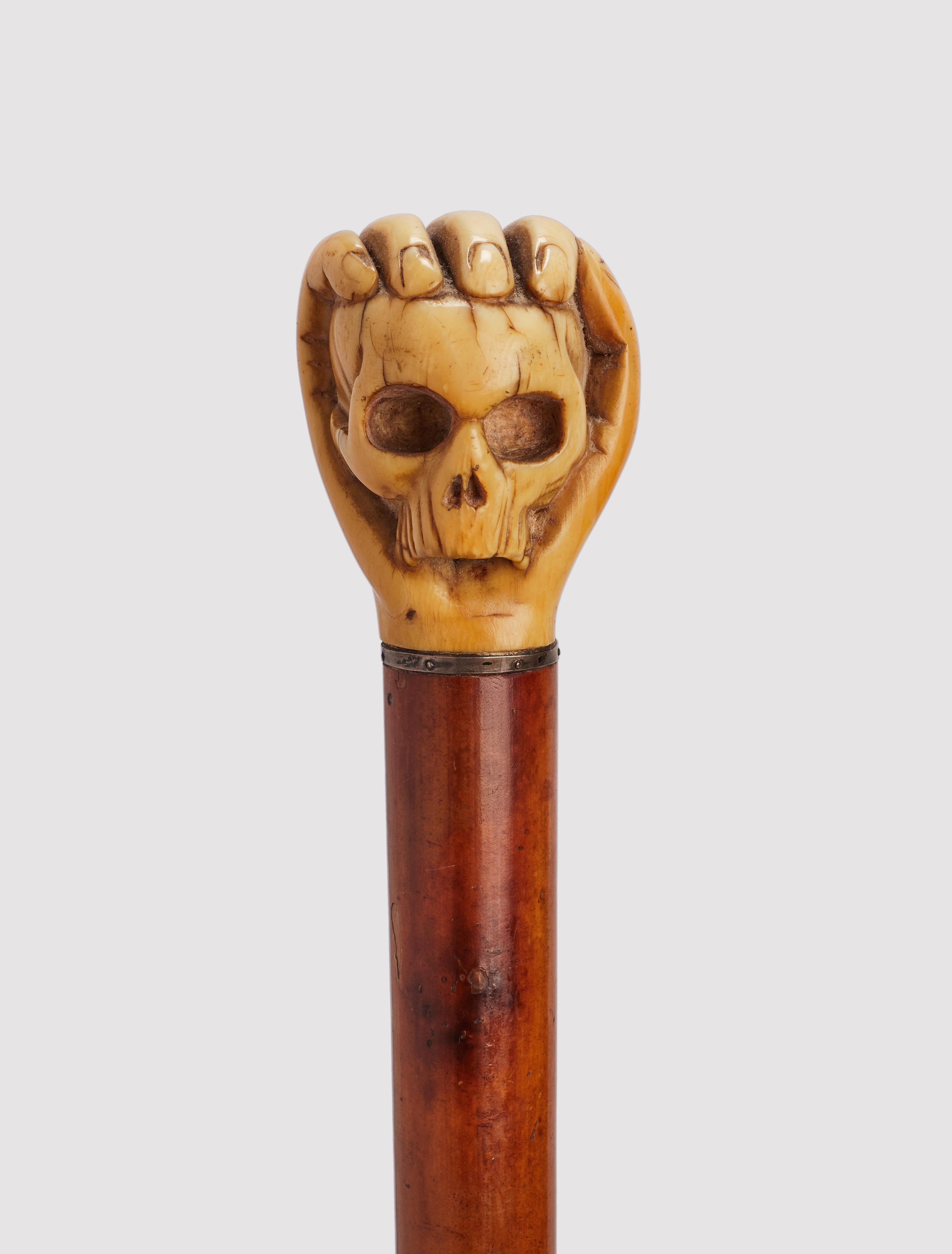 Walking stick: ivory carved handle, depicting a Memento Mori, a hand holding a skull. Malacca wood shaft. Silver ring. Horne ferrule. Germany circa 1860. (SHIP TO EU ONLY)