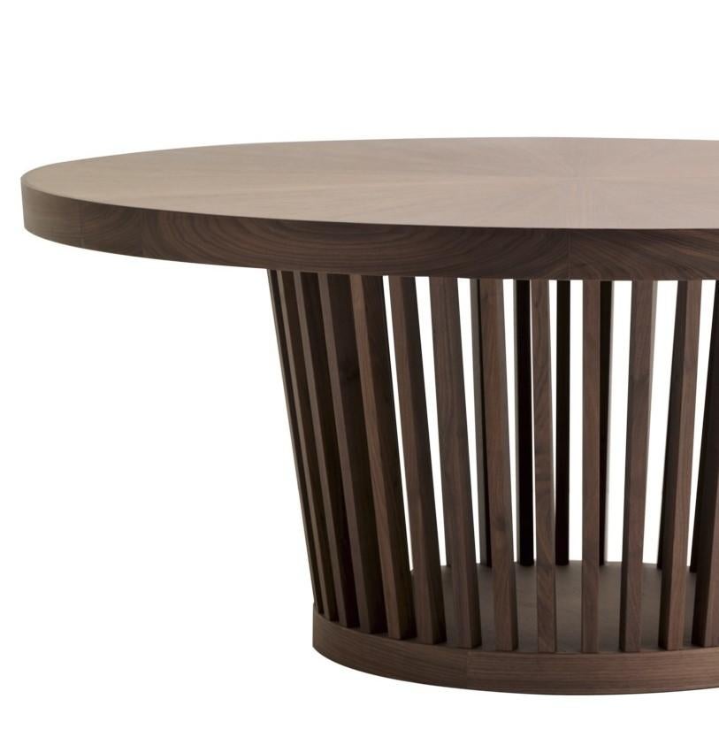 This sophisticated dining table has a round top in walnut-veneered wood, supported by an exquisite structure made entirely in solid walnut wood and comprised of thin slats vertically rising to the top from a small round base. This design, simple and