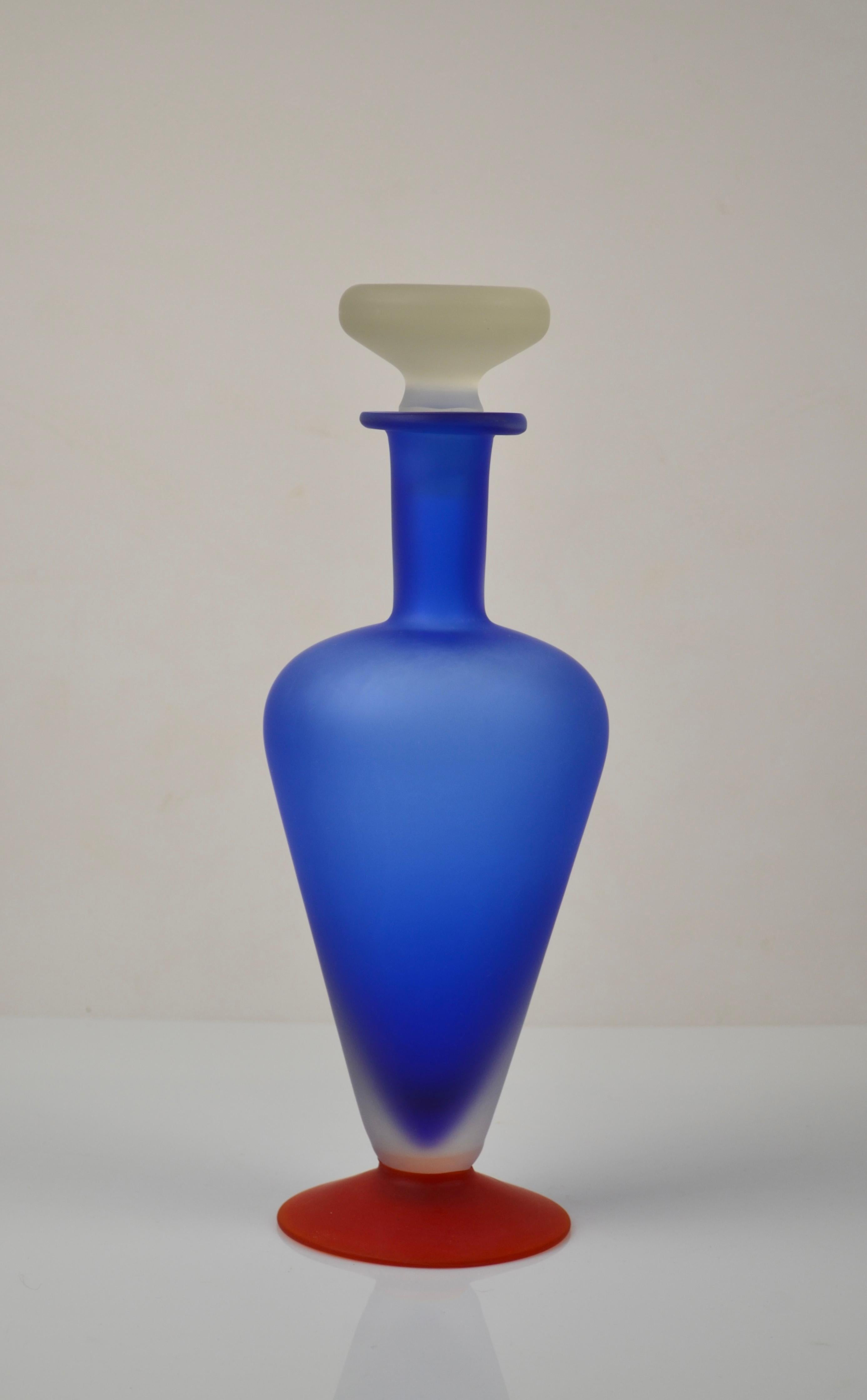 Striking sculptural decorative bottle in hand-blown frosted art glass, featuring a bold cobalt blue gradient body resting on a vivid red base and topped with an opaque white sculptural stopper. The strong geometric composition and playful color