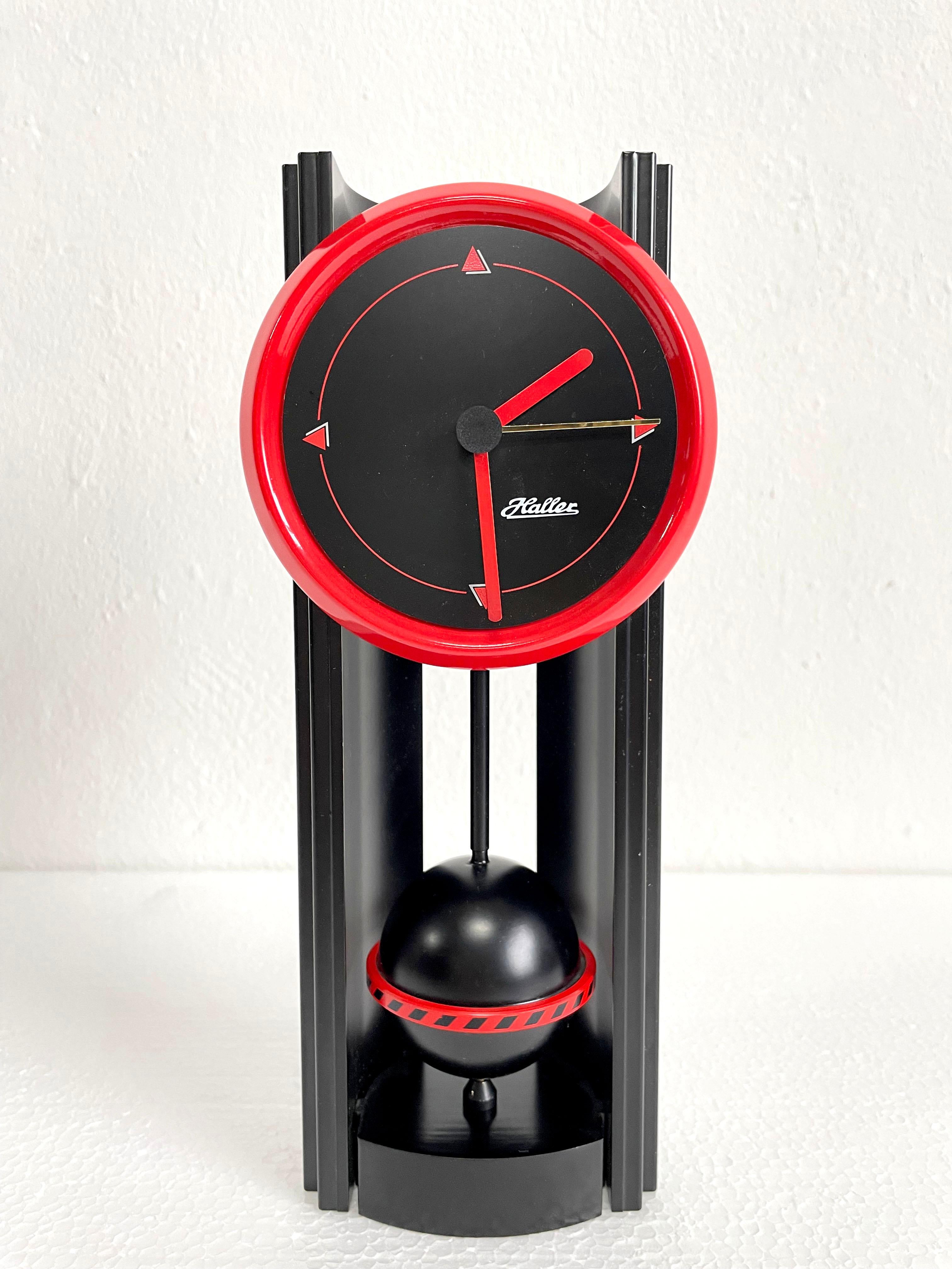 Seltene Tischuhr im Memphis-Stil, hergestellt in den 1980er Jahren in Deutschland von Haller Clocks.

Die Uhr ist aus schwarzem und rotem Kunststoff gefertigt und hat einen batteriebetriebenen Mechanismus für eine Batterie des Typs AA. Es ist in