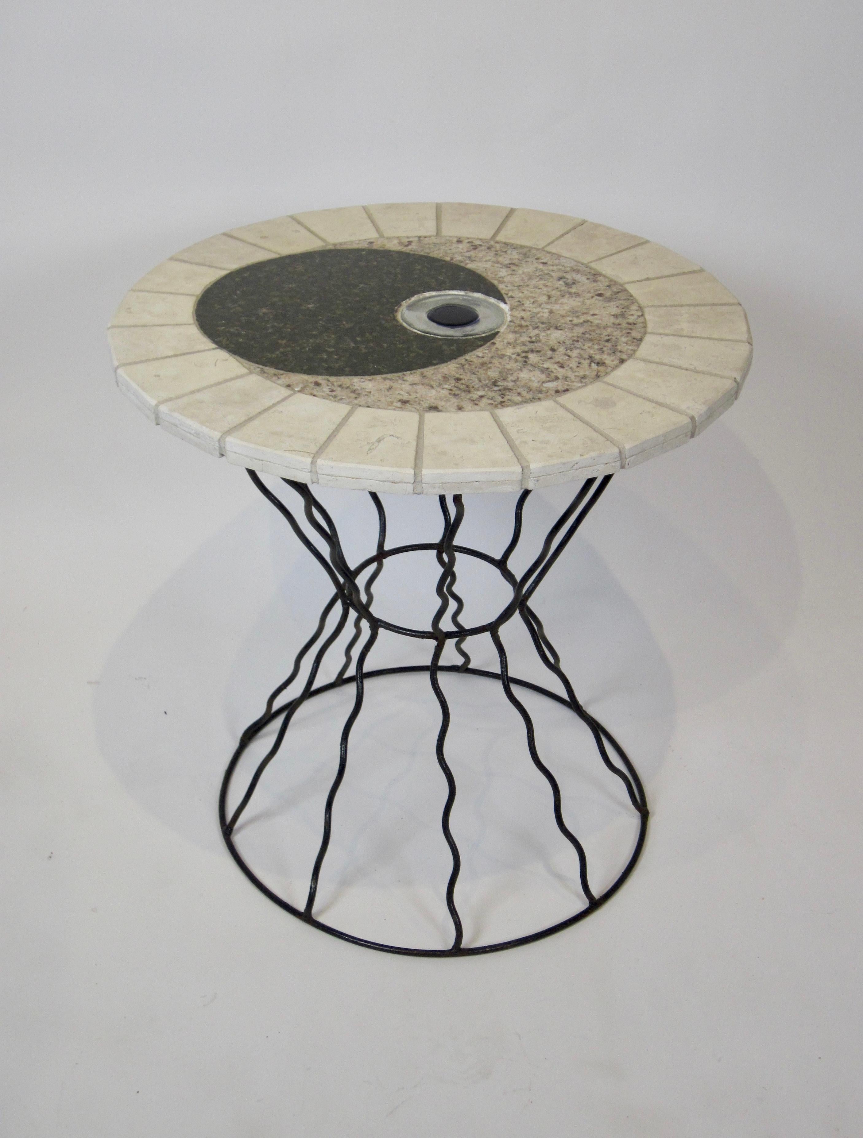 Round studio made top with travertine, granite, and glass. The top is supported by undulating wire rods gathered at the center creating a pinched waist. The two together bring to mind a modern Memphis design with a third eye feel. That is what I