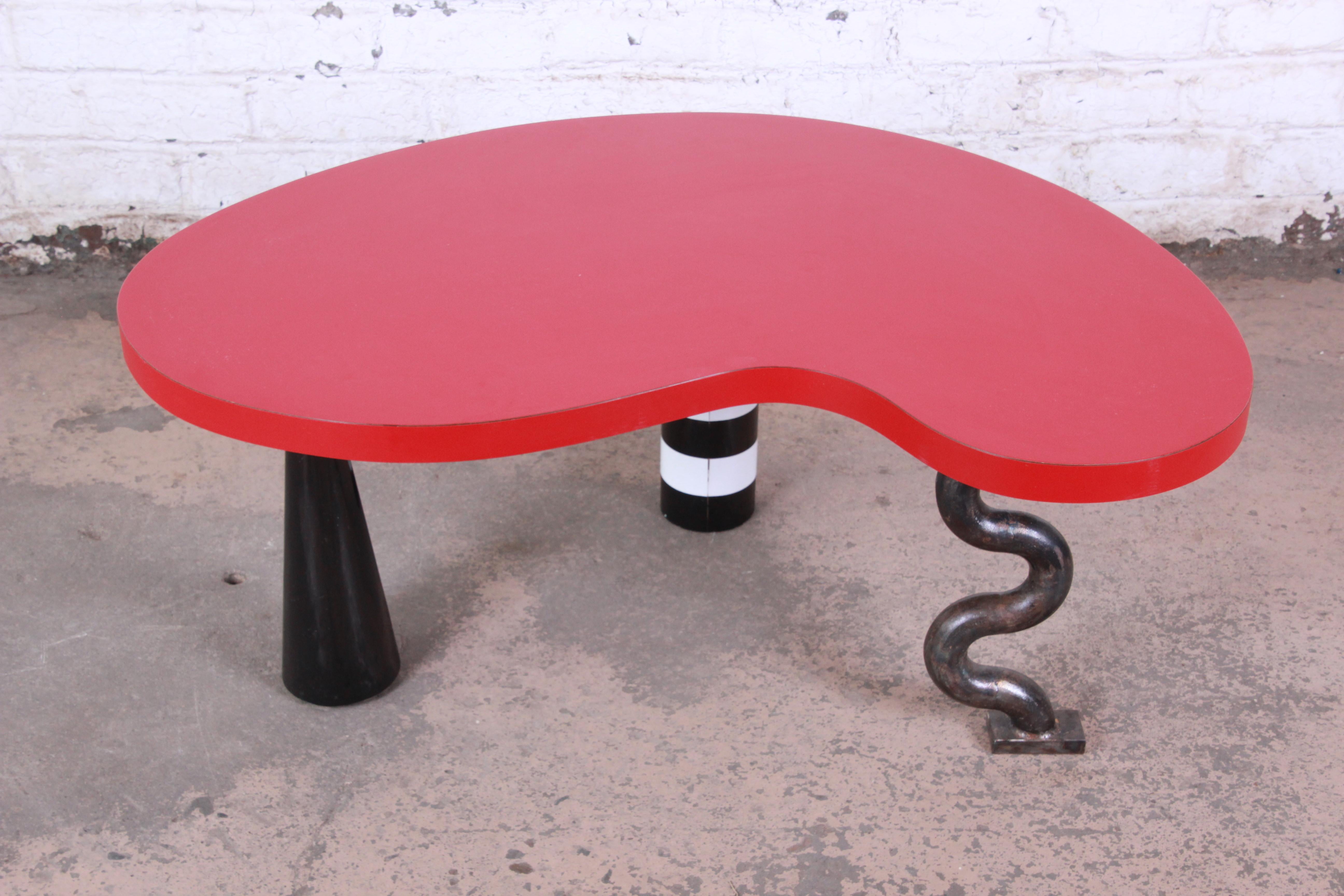 A rare and unusual kidney shape cocktail table in the manner of Ettore Sottsass for Memphis Group. The table features three unique custom designed legs and a red laminate kidney-shaped tabletop. The table was made circa 1980s and is in good original