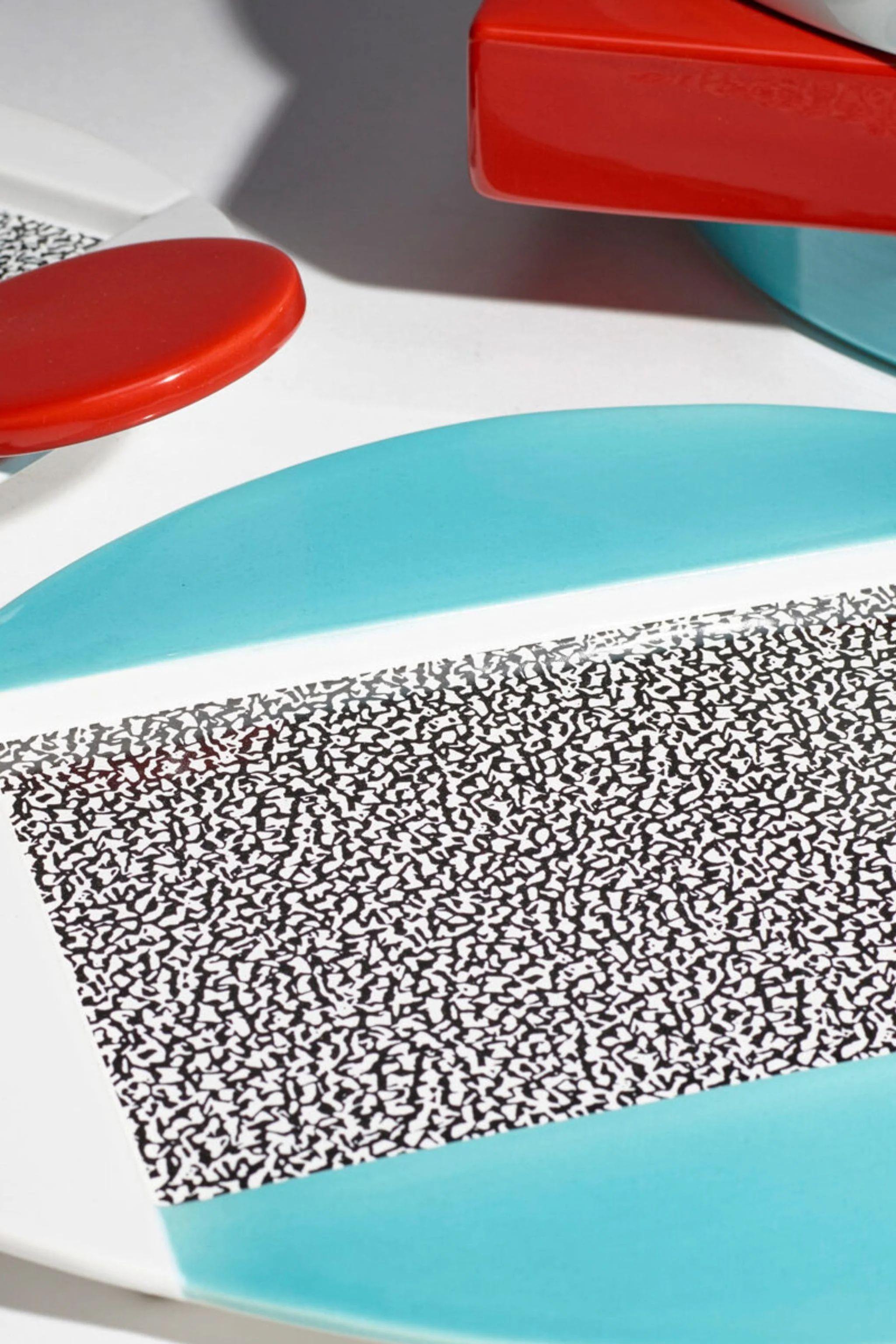 Michele De Lucchi décore Celery, un plat de service en céramique avec des motifs géométriques et des figures. Il travaille sur la juxtaposition de figures simples : dans la partie centrale, un rectangle réalisé à l'aide d'un décalque décoratif