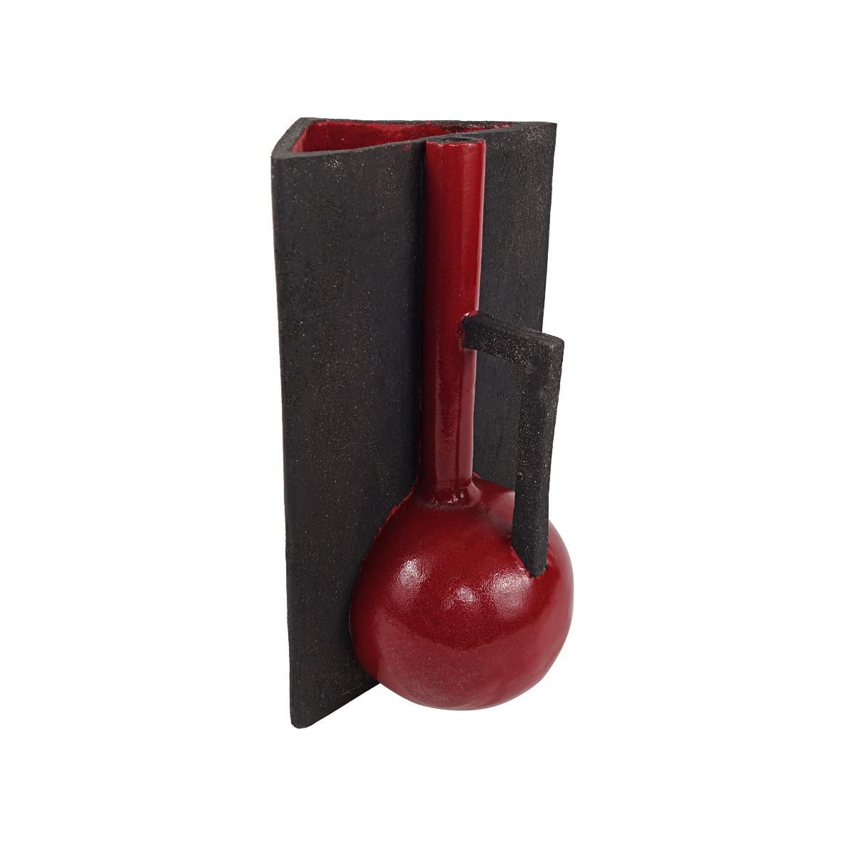 This ceramic vase is actually composed of two vases riveted together, having each their own shape, color and style. One is triangular matte black and handleless and only glazed on the inside. The other is round, and shiny red matte with a square