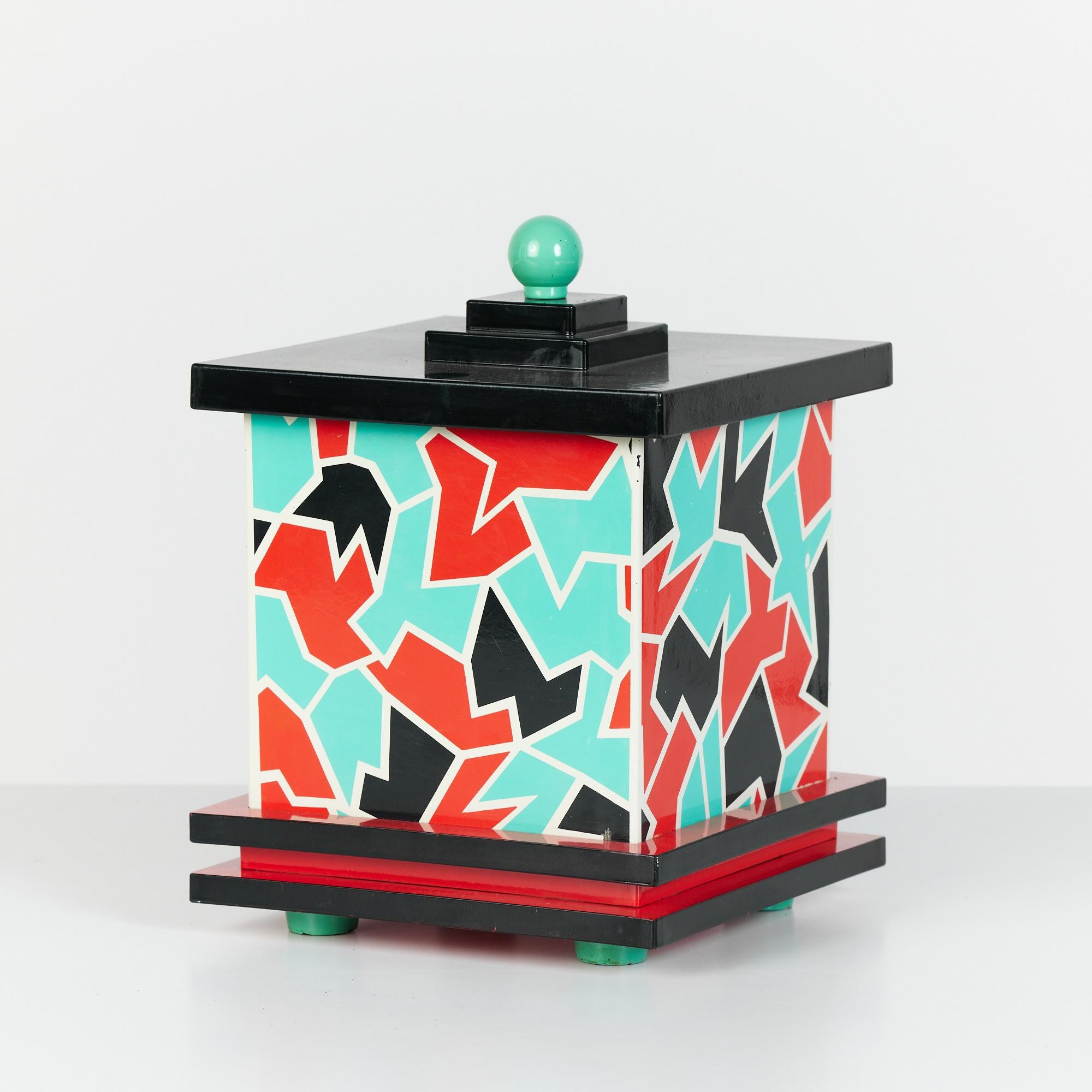 A lidded post modern Memphis ice bucket for Taste Seller, c.1980s, Japan. The bucket features and geometric black red and teal pattern with cream outlining. The black lid has three tiers and is finished with a teal globe pull. The base of bucket is