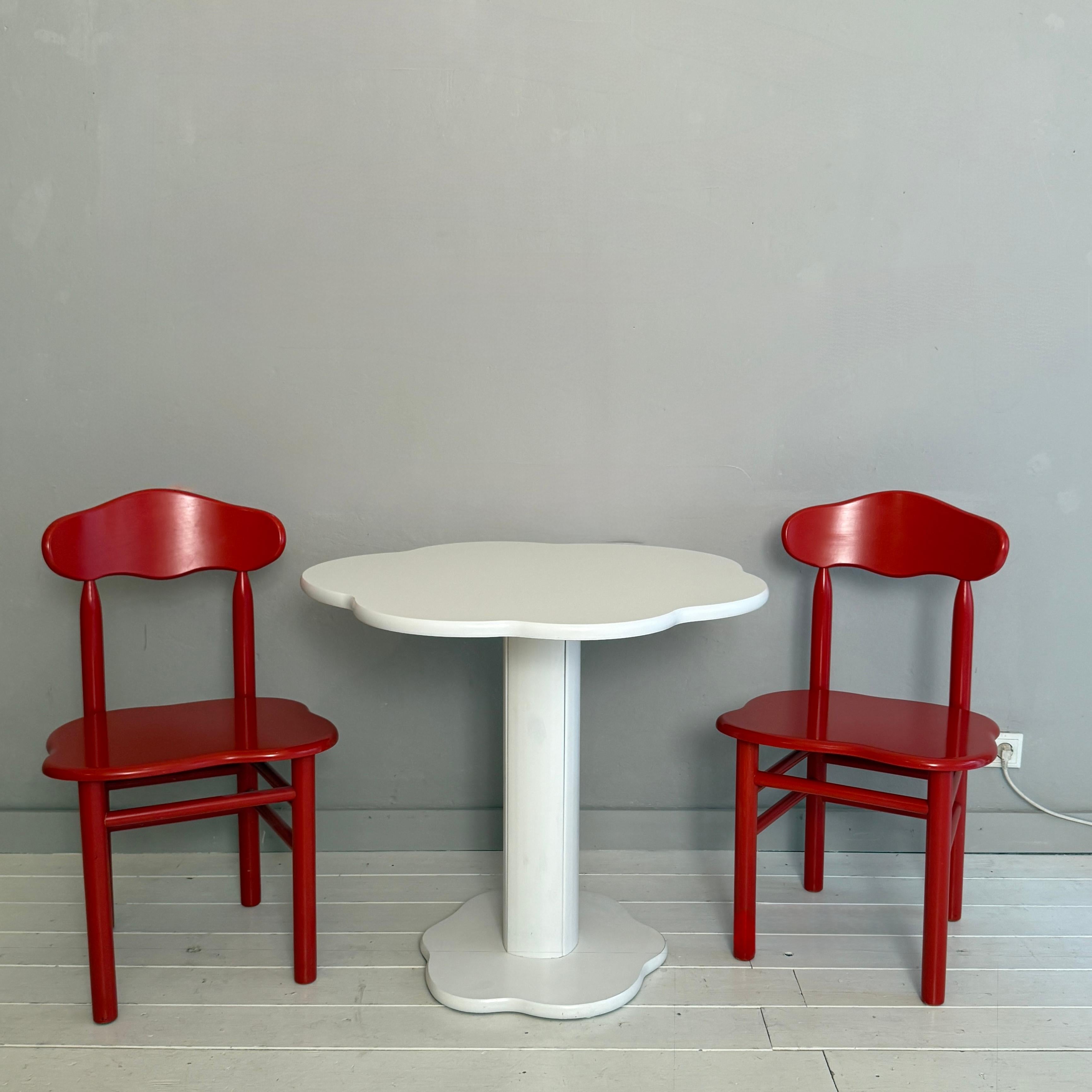 This playful Memphis-style set, created around 1990, consists of two sculptural chairs and a matching table in a charming cloud-inspired design. The chairs feature bold red lacquered frames with whimsically contoured backrests and seats, capturing