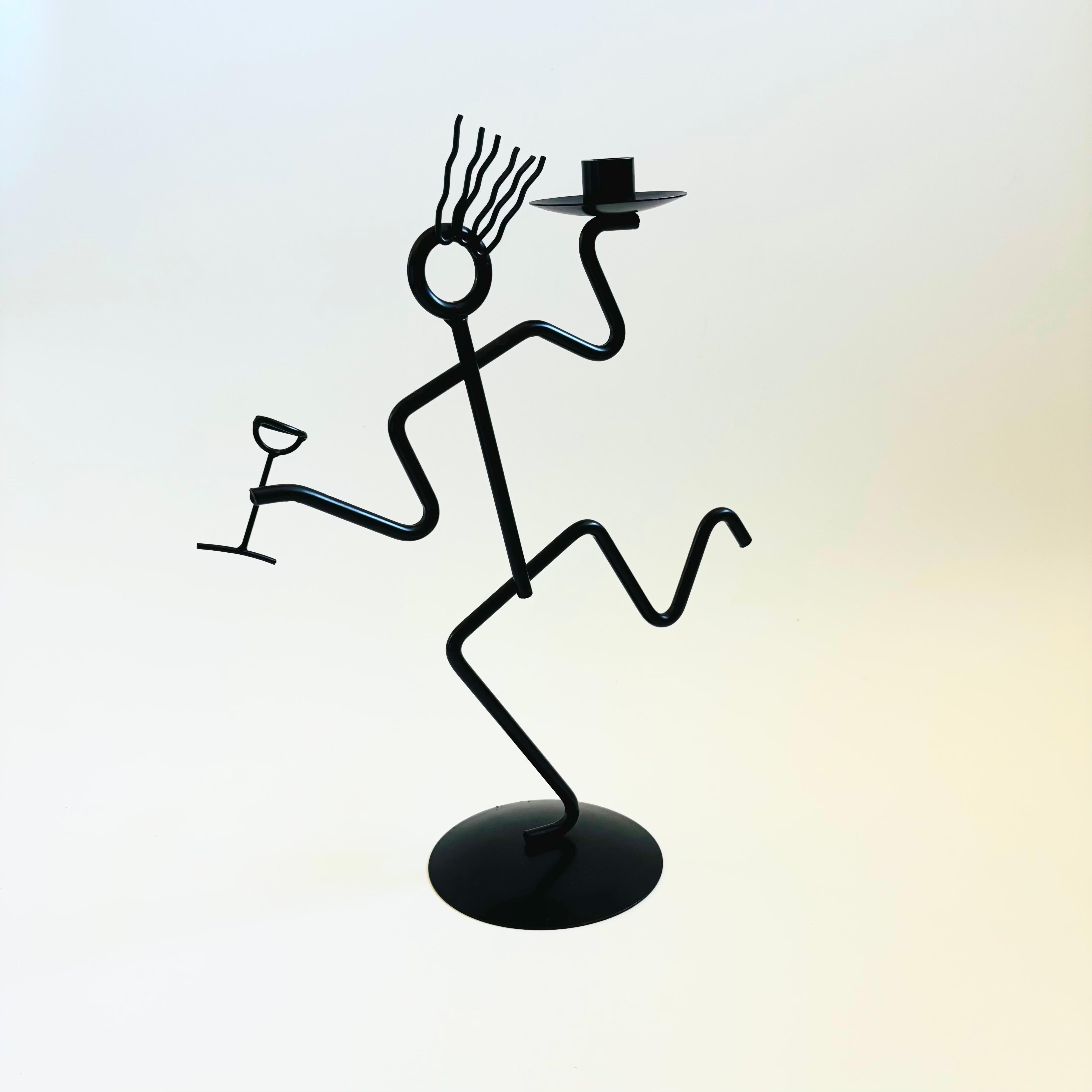 Un portacandele vintage degli anni '80 in stile memphis in metallo nero. La persona con il bastone tiene un bicchiere di vino in una mano e nell'altra mano c'è un portacandele. Capelli mossi eccentrici. Un grande pezzo vintage postmoderno. MEAN è