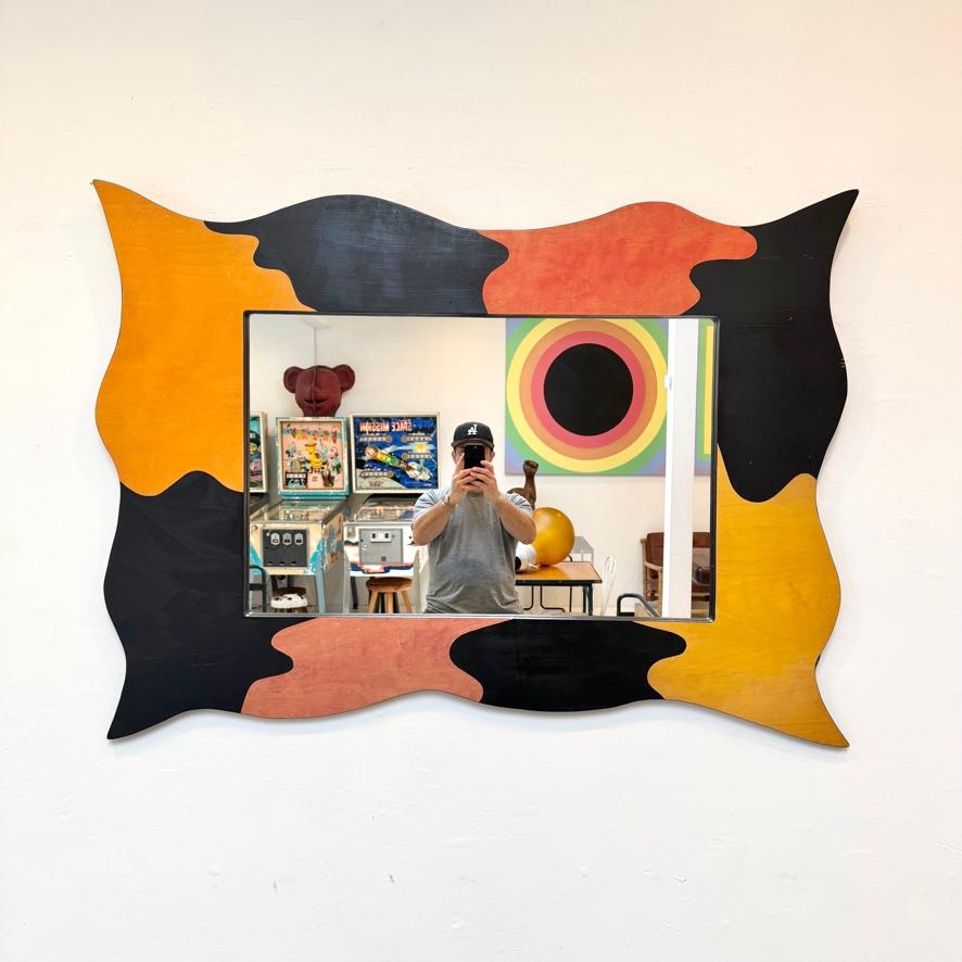 This mirror is maximalist heaven. Handmade in the late 20th century and influenced by the Memphis Design style, it features bold colors and silhouettes, With wavy edges and pointed corners, the frame is decorated with improvised blocks of orange,