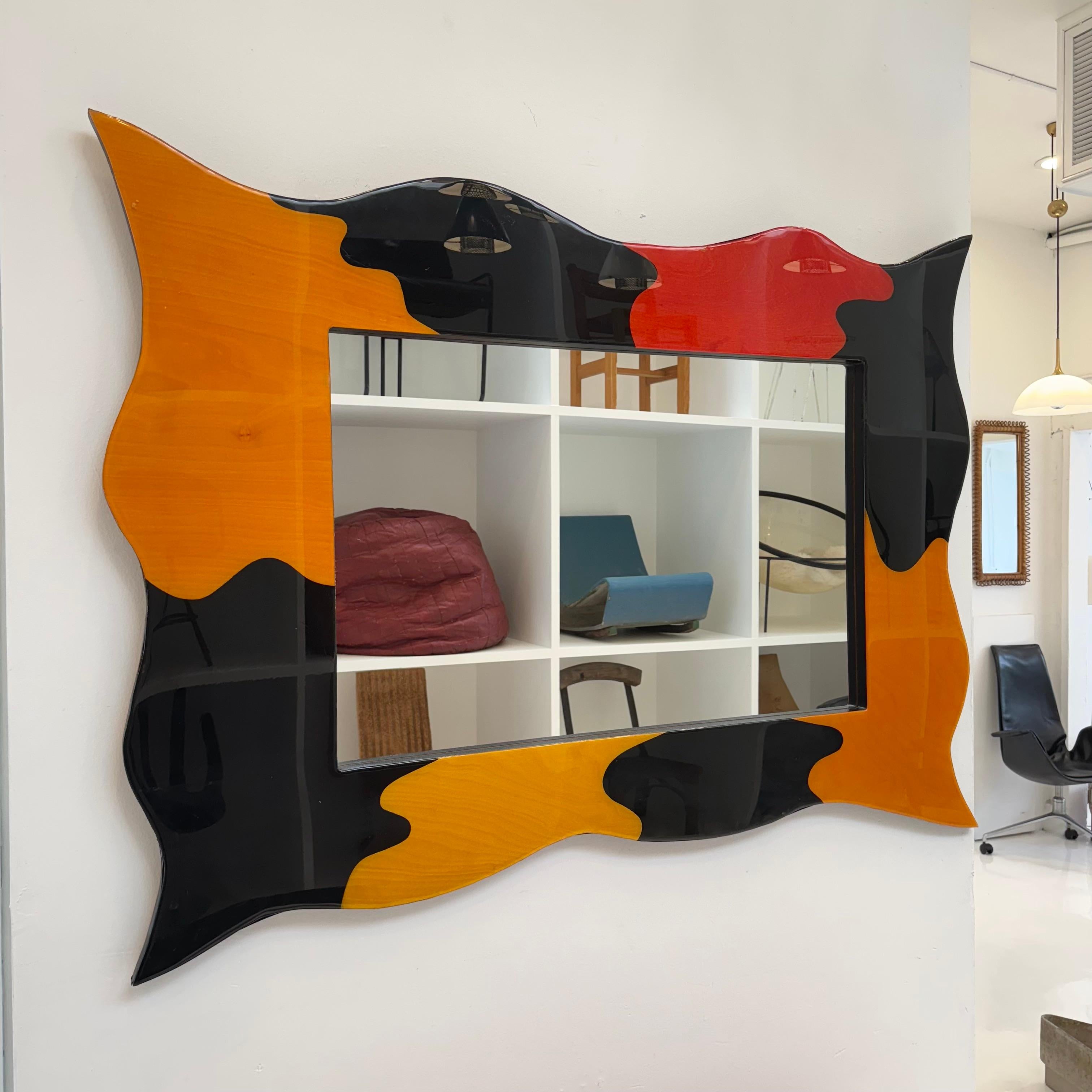 This mirror is maximalist heaven. Handmade in the late 20th century and influenced by the Memphis Design style, it features bold colors and silhouettes, With wavy edges and pointed corners, the frame is decorated with improvised blocks of orange,
