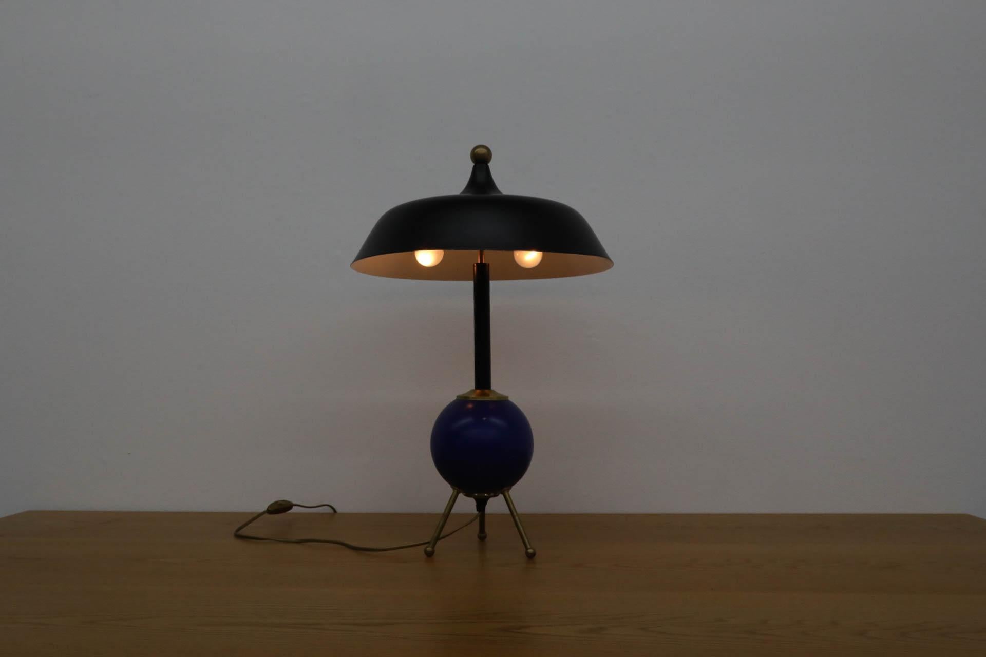 Fun Ettore Sottsass inspired table lamp with a large cobalt blue lacquered wood ball body supported by brass tripod legs and a middle eastern style black enameled metal shade. In original condition with visible wear including some paint loss to the