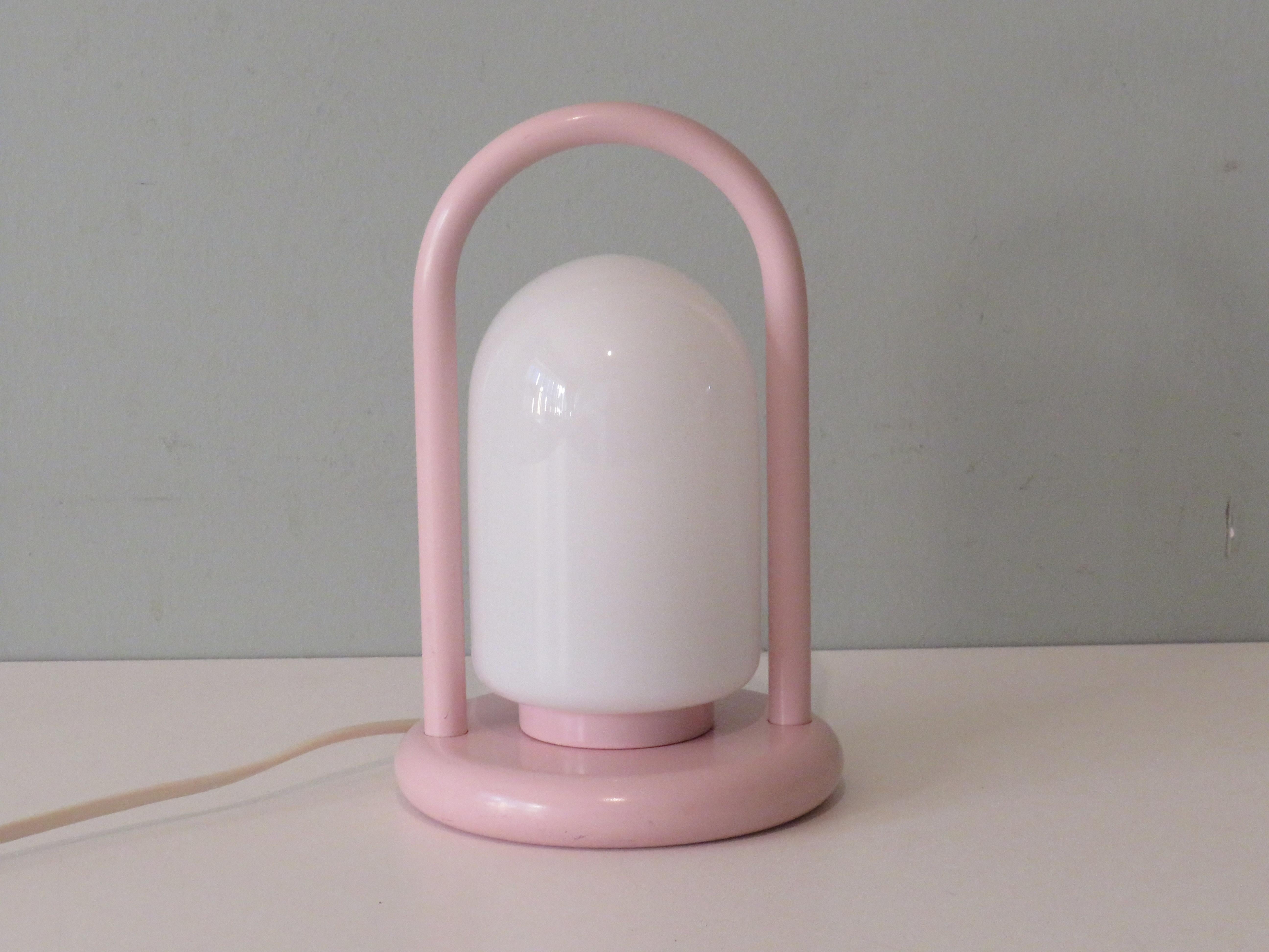 The table lamp has a pink metal frame and a white glossy opaline chalice. It is manufactured by Massive, Belgium and provided with a label. It is equipped with 1 E 14 fitting and an on and off button on the cord.
It can be used for both 110-150 V