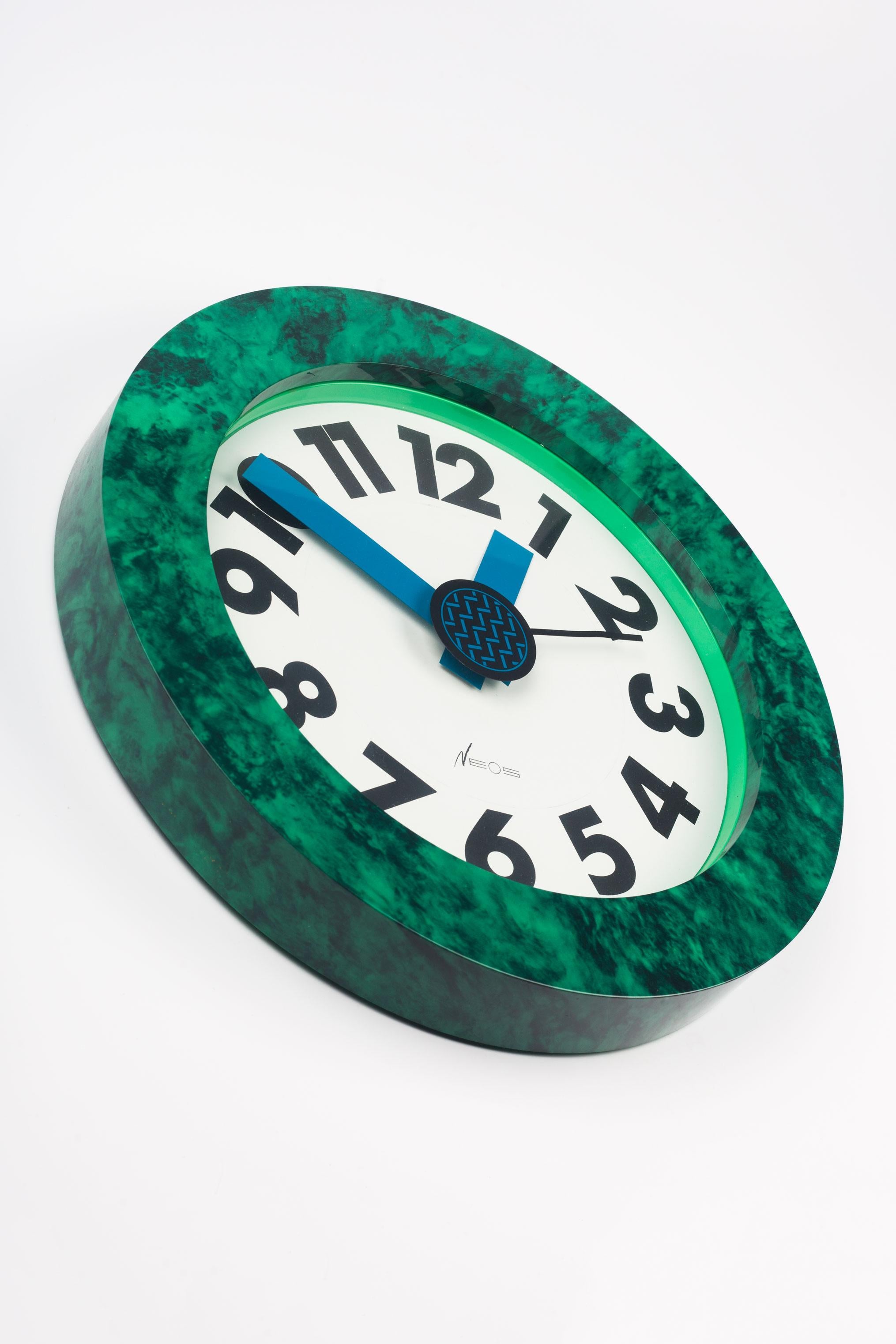 Postmodern wall clock designed by the Memphis Group founding members and couple, George Sowden and Nathalie du Pasquier. Marbled green and black pattern frame with bold black numerals behind thick, crisp, blue hour and minute hands. The central