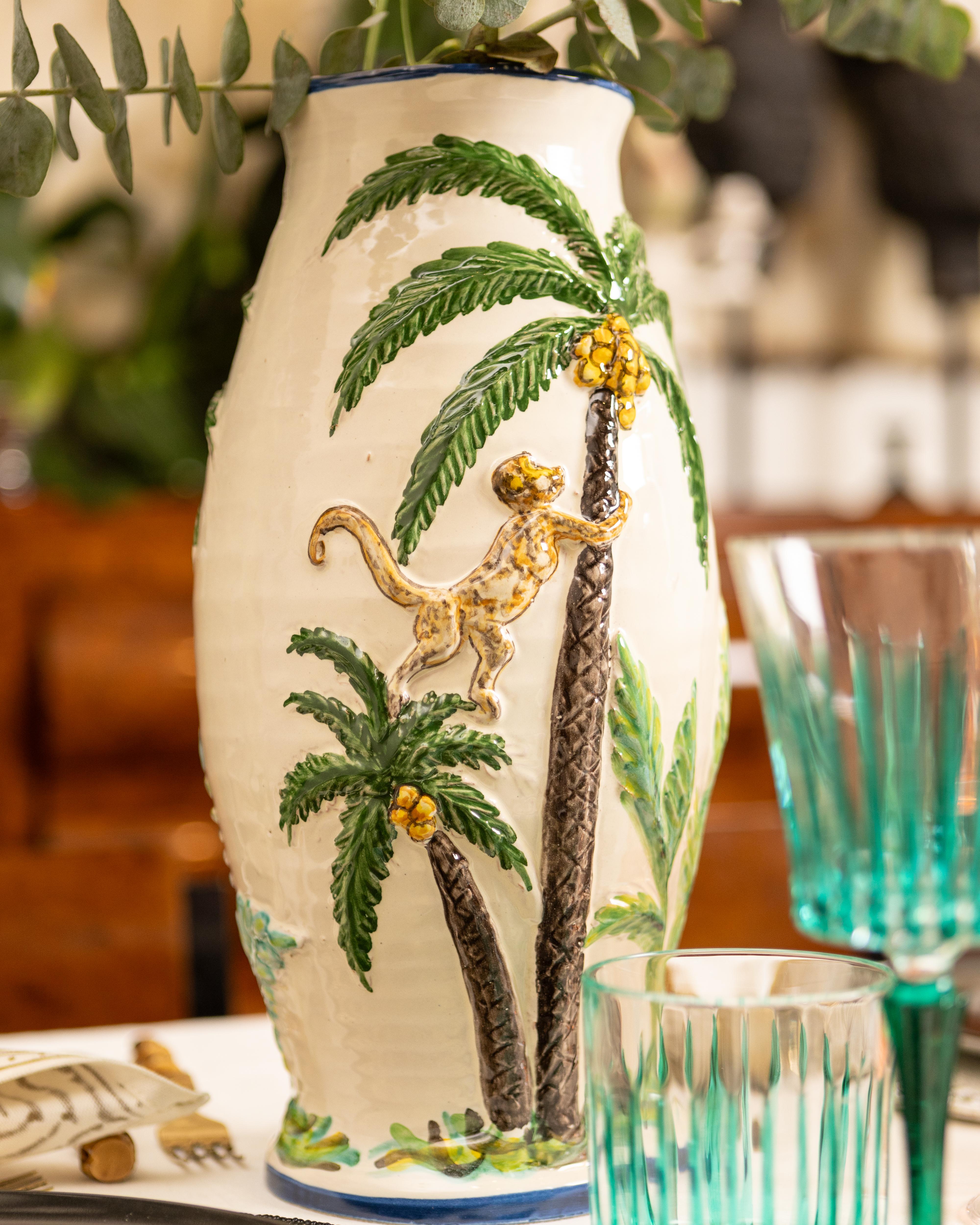 Verleihen Sie Ihrem Zuhause verspielte Eleganz mit der handbemalten Keramikvase Menagerie. Diese bezaubernde Vase zeigt einen Affen, der anmutig auf eine Palme klettert. Sie bringt tropische Wärme und skurriles Flair in Ihr Interieur. Jede Vase wird