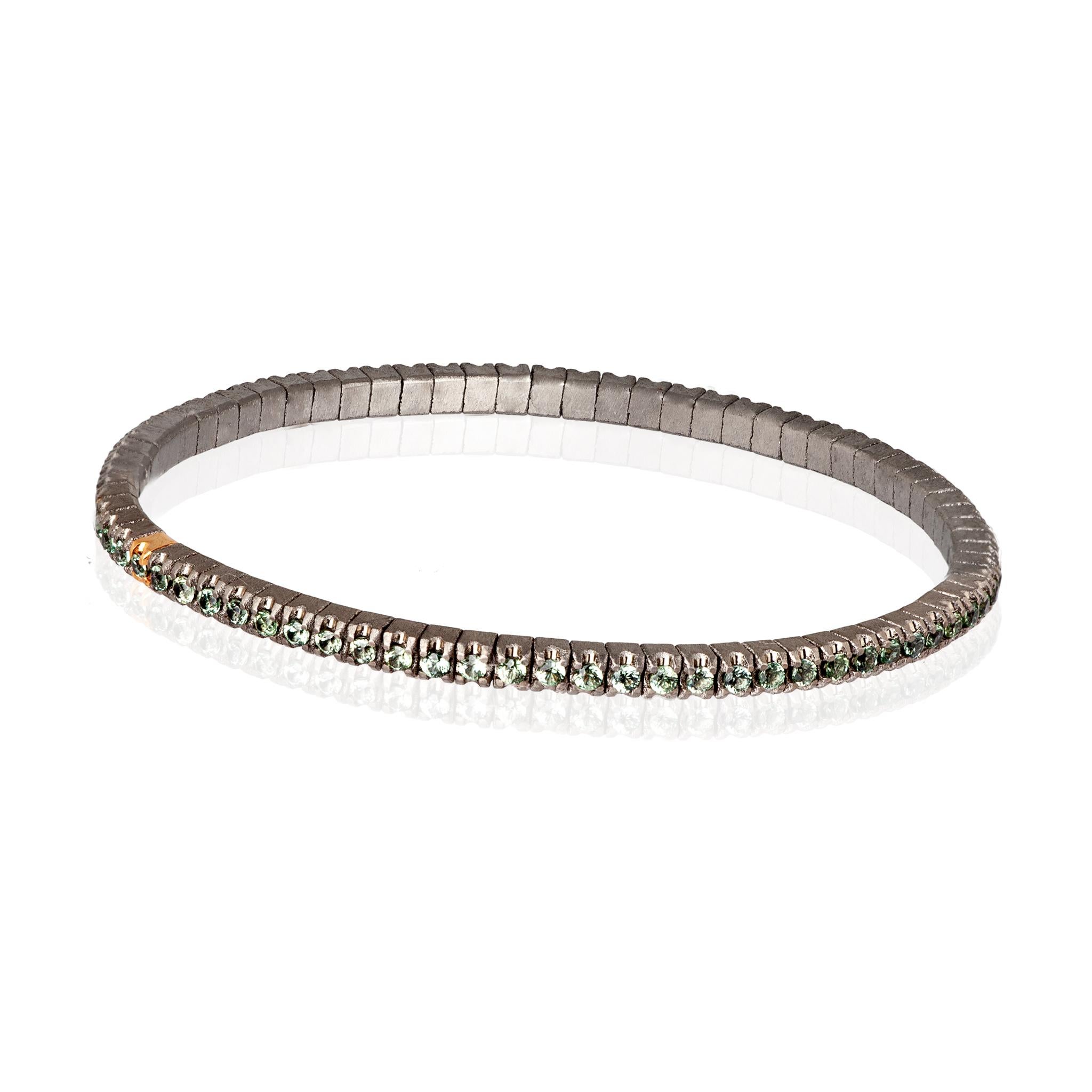 Men's Line Loop bracelet in titanium and green sapphires (ct. 2.15 approx.). The structure consists of an unbroken row of 3-point diamonds set on titanium griffes and one in 18kt red gold placed side by side on an elastic link. This bracelet