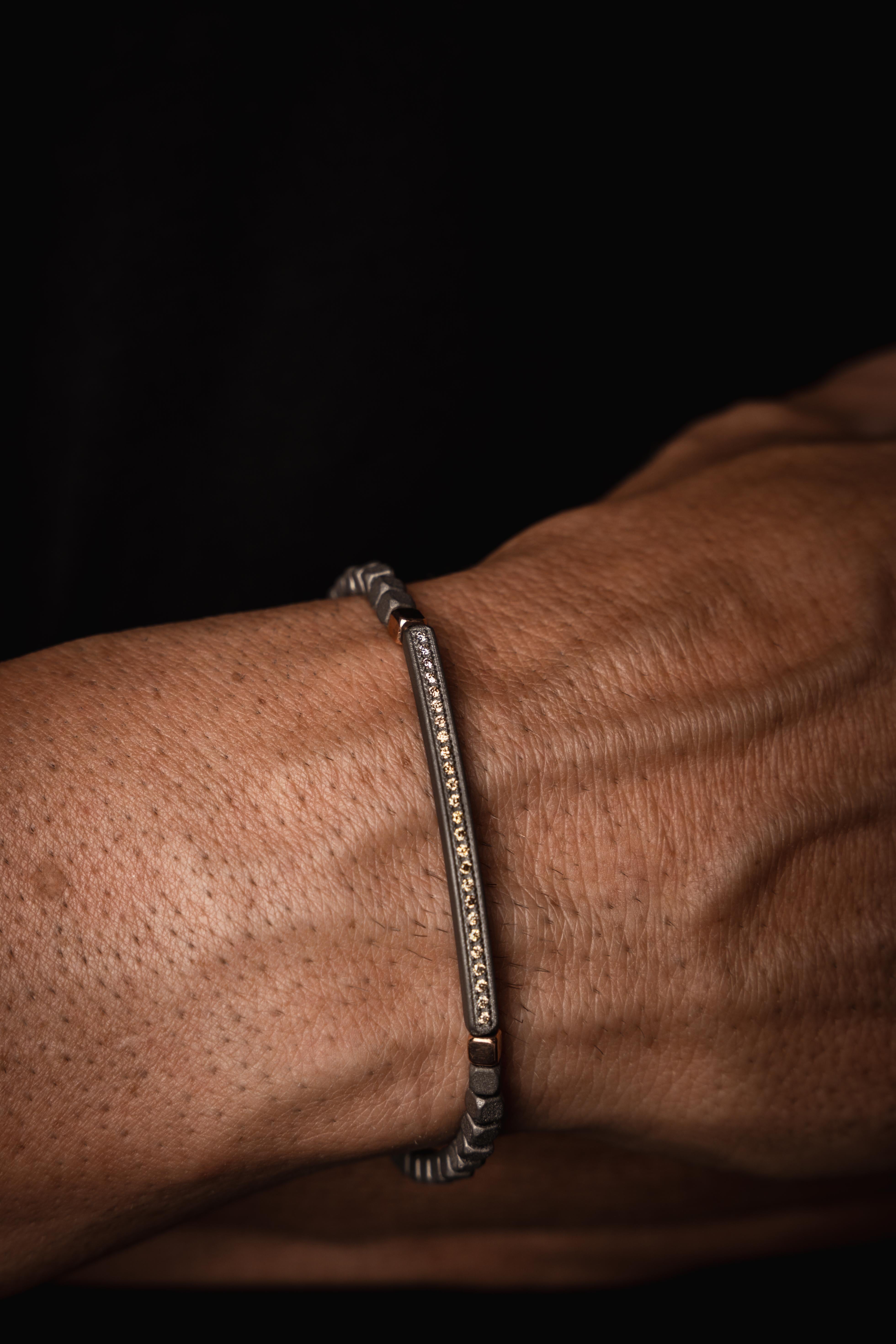 Men's titanium bracelet, 25 white diamonds, 2 9 kt red gold cubes at the ends of the bar and 9 kt red gold rings with 9 kt red gold clasp and a titanium cornet dangling from the last ring. A titanium bar, on which 25 1-point white diamonds are set