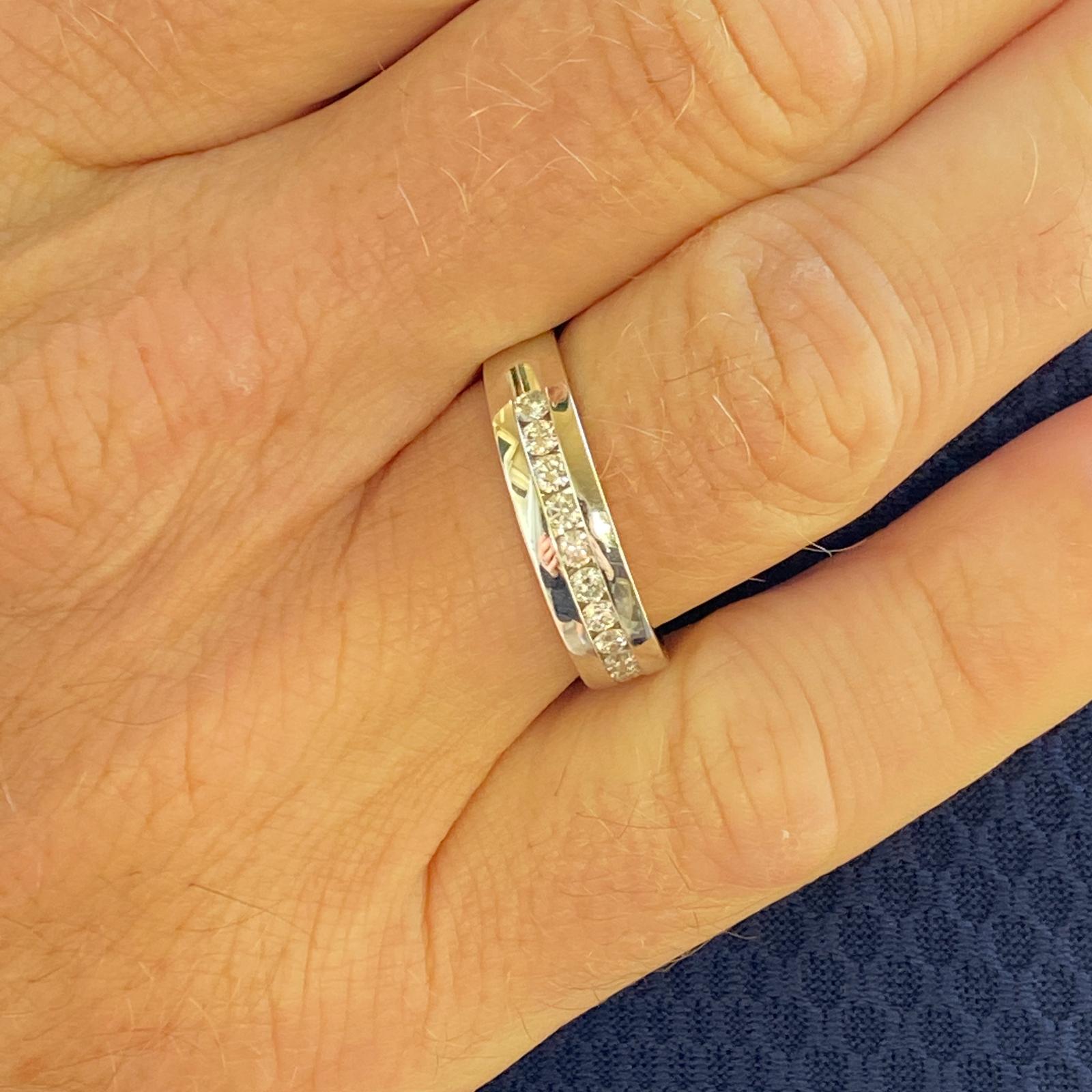 Gents diamond band ring fashioned in 14 karat white gold. The band features 11 channel set round brilliant cut diamonds weighing .55 carat total weight and graded G-H color and SI clarity. The band measures 5.5mm in width and is size 10. 