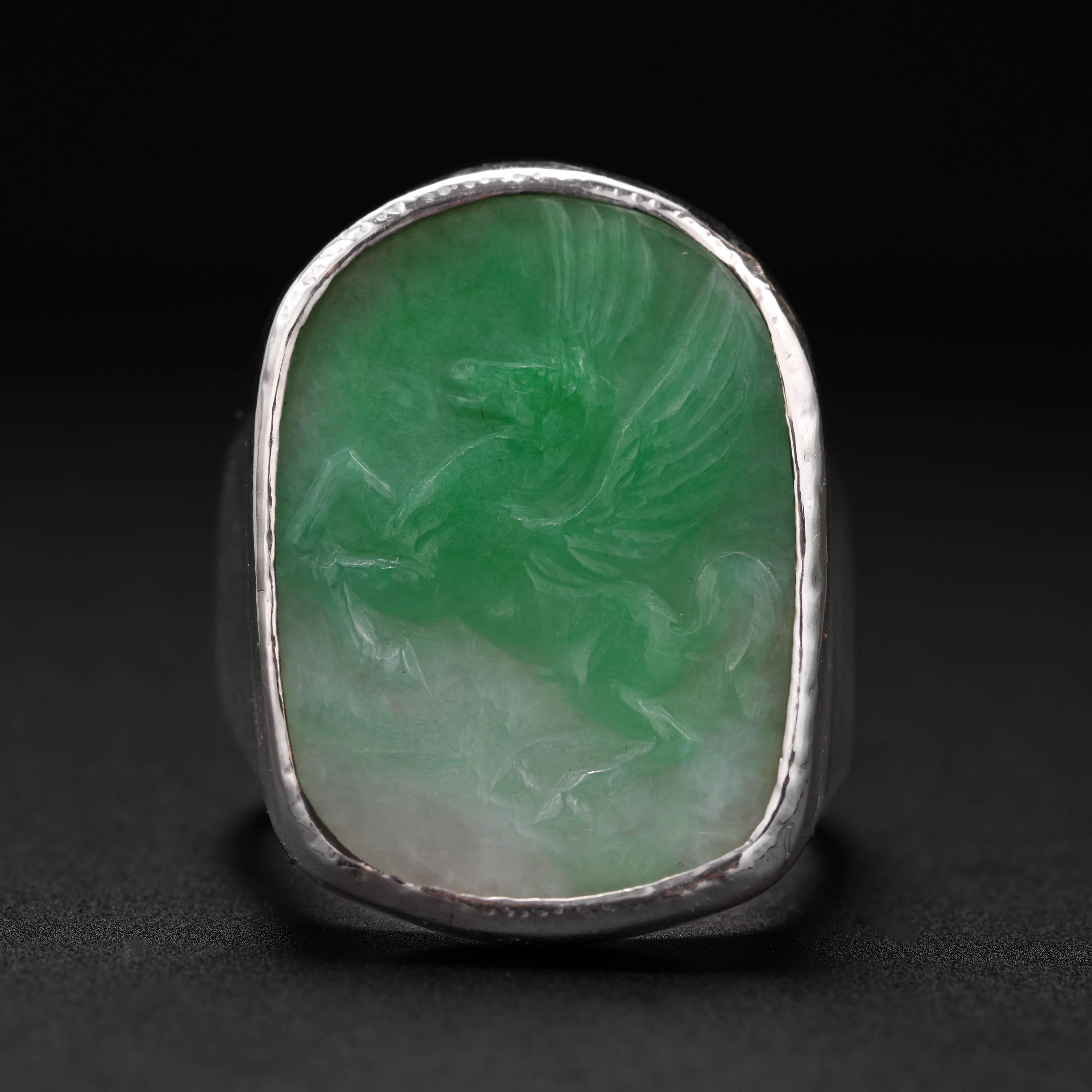 A plaque of moss-on-snow natural and untreated Burmese jadeite jade has been intricately, impeccably hand-carved to depict Pegasus; the winged horse from Greek Mythology. The freeform-shaped plaque is bezel-set within a custom setting made to fit