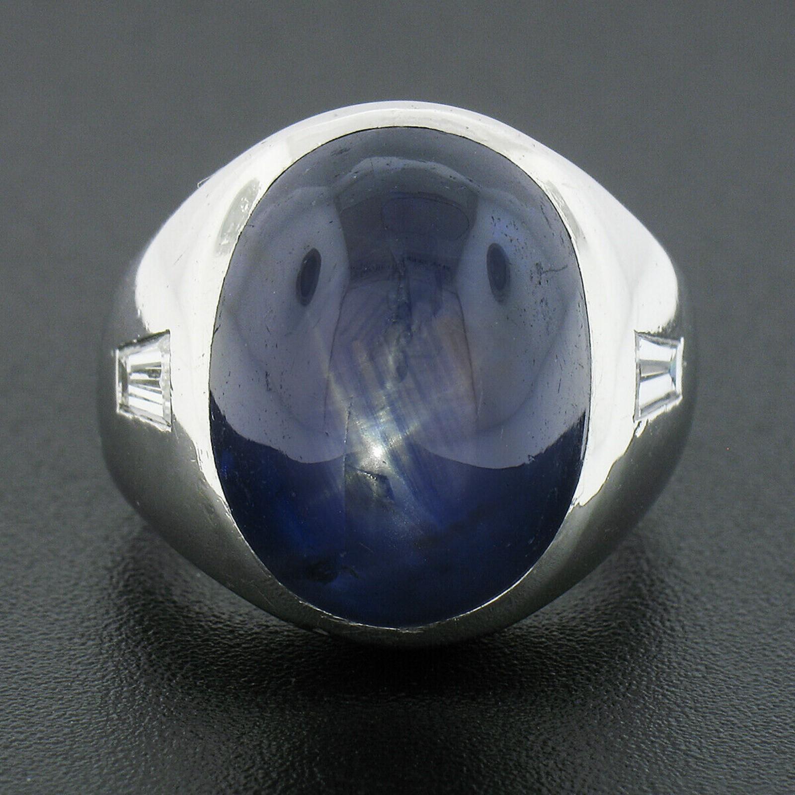 This large and heavy men's statement ring is crafted in solid platinum and features a magnificent, GIA certified, natural star sapphire bezel set at its center. The sapphire has rich and very desirable royal blue color with a well centered and