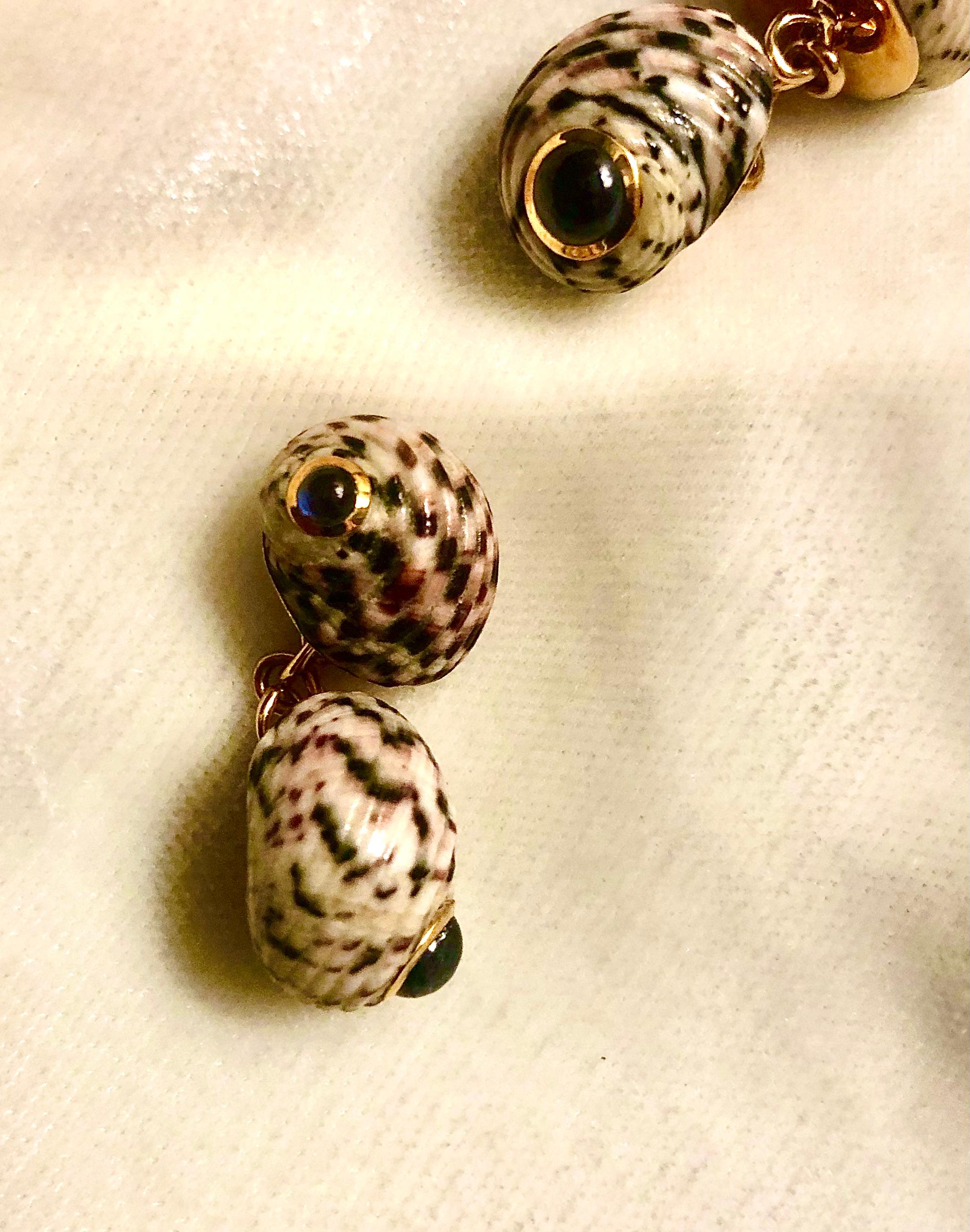 Magnifiques boutons de manchette Trianon (Seaman Schepps) vintage. Les coquilles sont de belles taches brunes sur un fond crémeux. Les boutons de manchette sont sertis en or 18kt avec des saphirs bleus cabochon.

Ils sont soutenus par une monture en