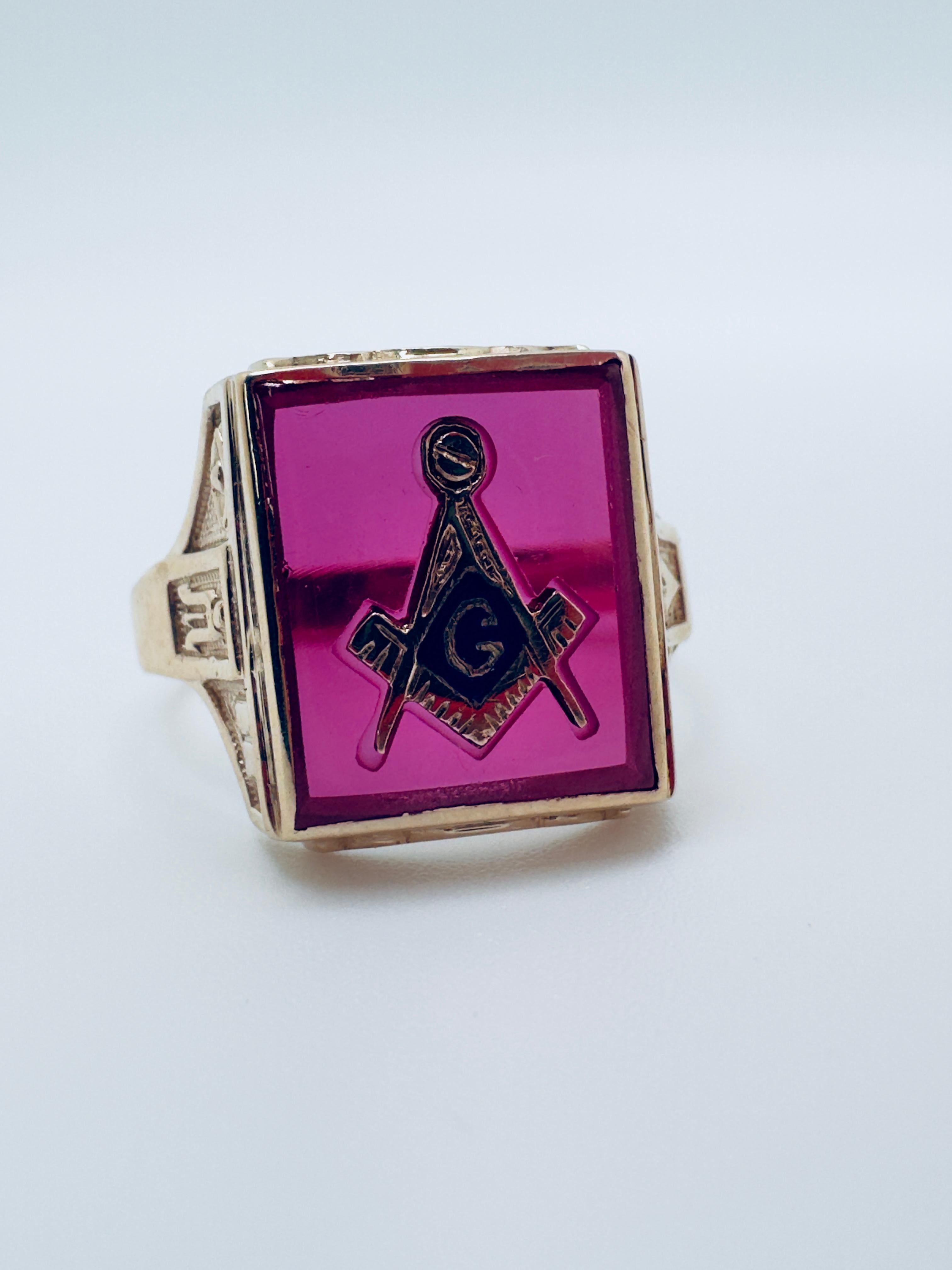 Questo anello massonico vintage da uomo è sapientemente realizzato in oro giallo 10 carati e mostra il distinto stile dei coperchi che emana tradizione e carattere. Al centro del disegno c'è una vibrante pietra rosso-rosa che funge da punto focale e