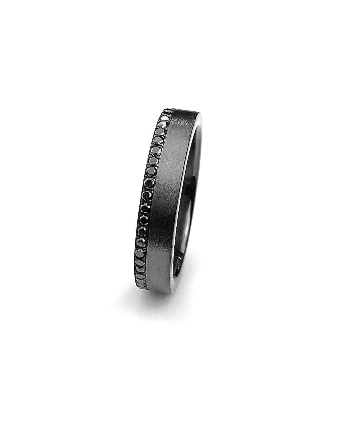 Men's wedding band in 18kt white gold, set with 0.10ct black diamonds off center on top surface of ring. Finished with light satin finish with black rhodium plating. Ring size 10.