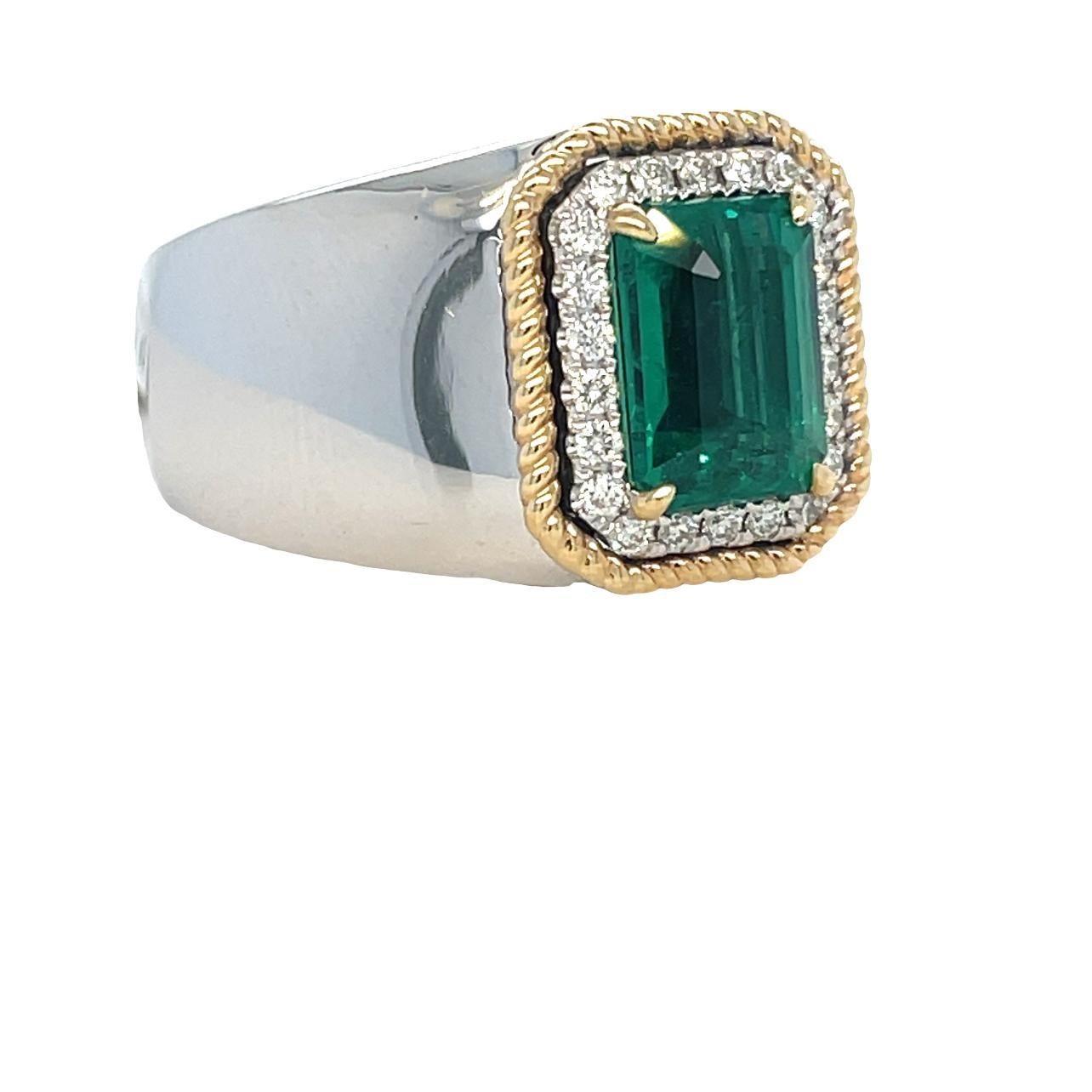This unique Two Tone Men's ring has a vibrant green 10x7 Emerald cut Zambian Emerald center surrounded by 22 brilliant cut round sparkling diamonds. The ring is set in 14K white and yellow gold. It comes in a beautiful box ready for the perfect