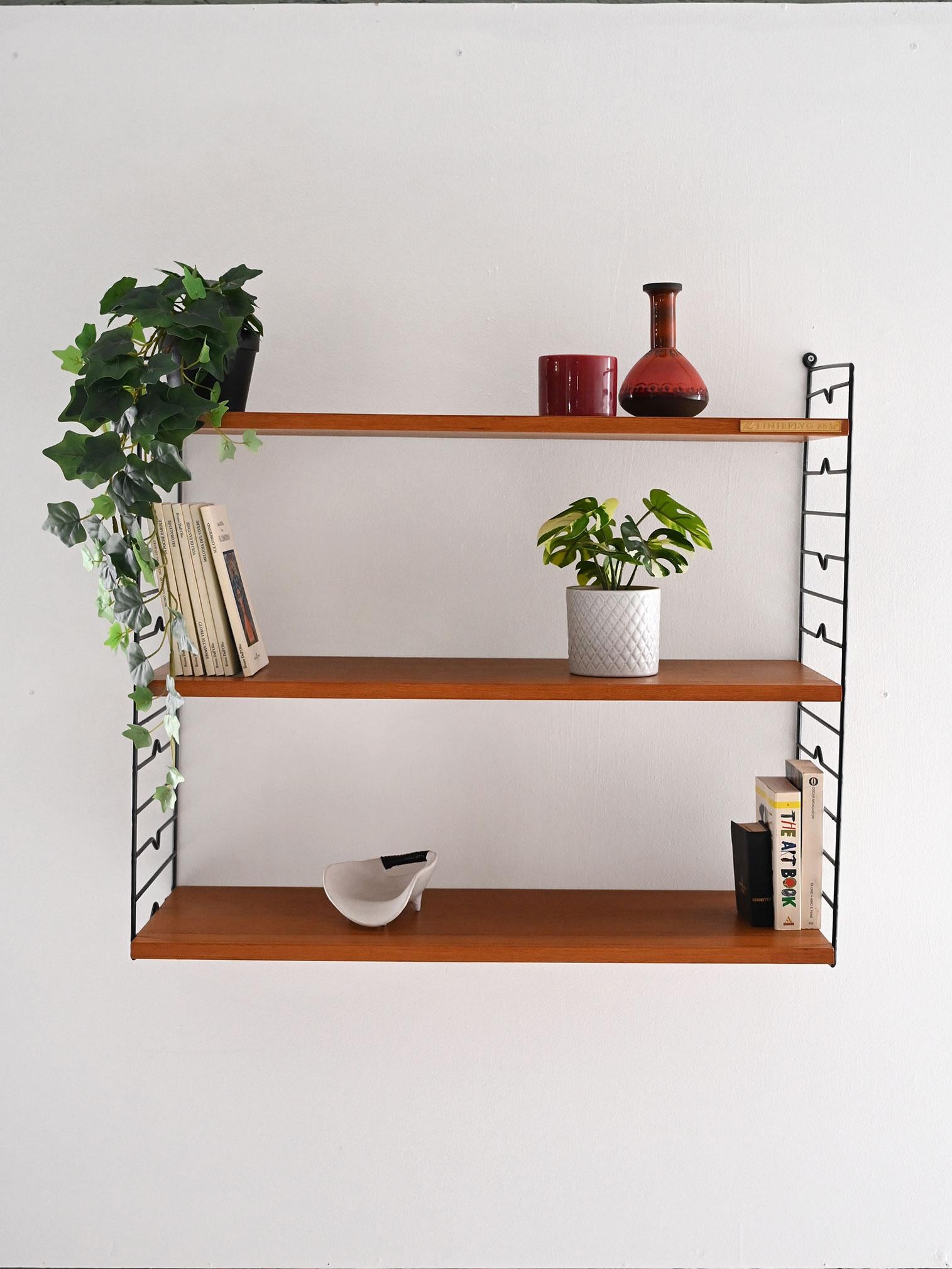 Sistema a muro vintage con mensole in teak regolabili e struttura in metallo nero decorata con motivo geometrico.

Sistema di mensole a muro “Hylla”, tipico del design funzionale scandinavo degli anni ’60. Questo modello vintage è dotato di tre