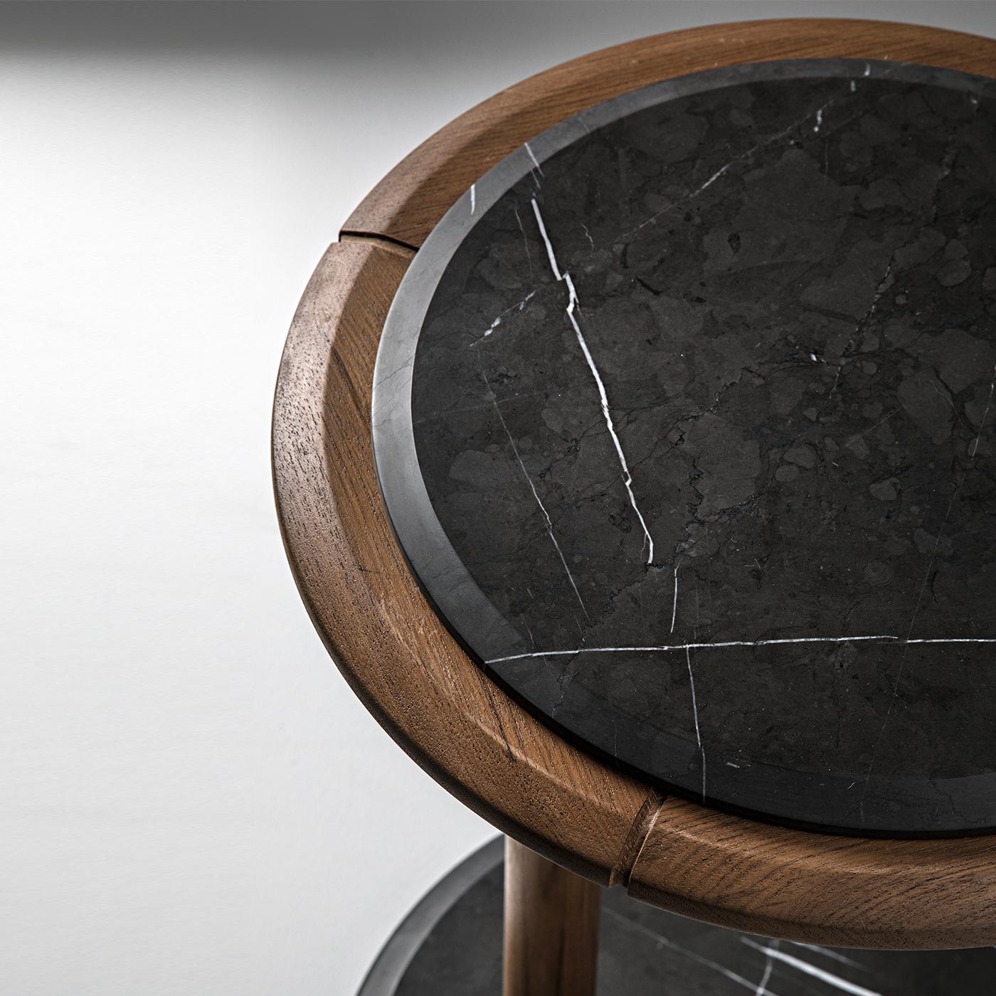 The durability and timeless charm of materials such as teak and black marble defines the elegant character infusing this round side table. Featuring structural details in nautical stainless steel, the design stands out for its asymmetrical profile
