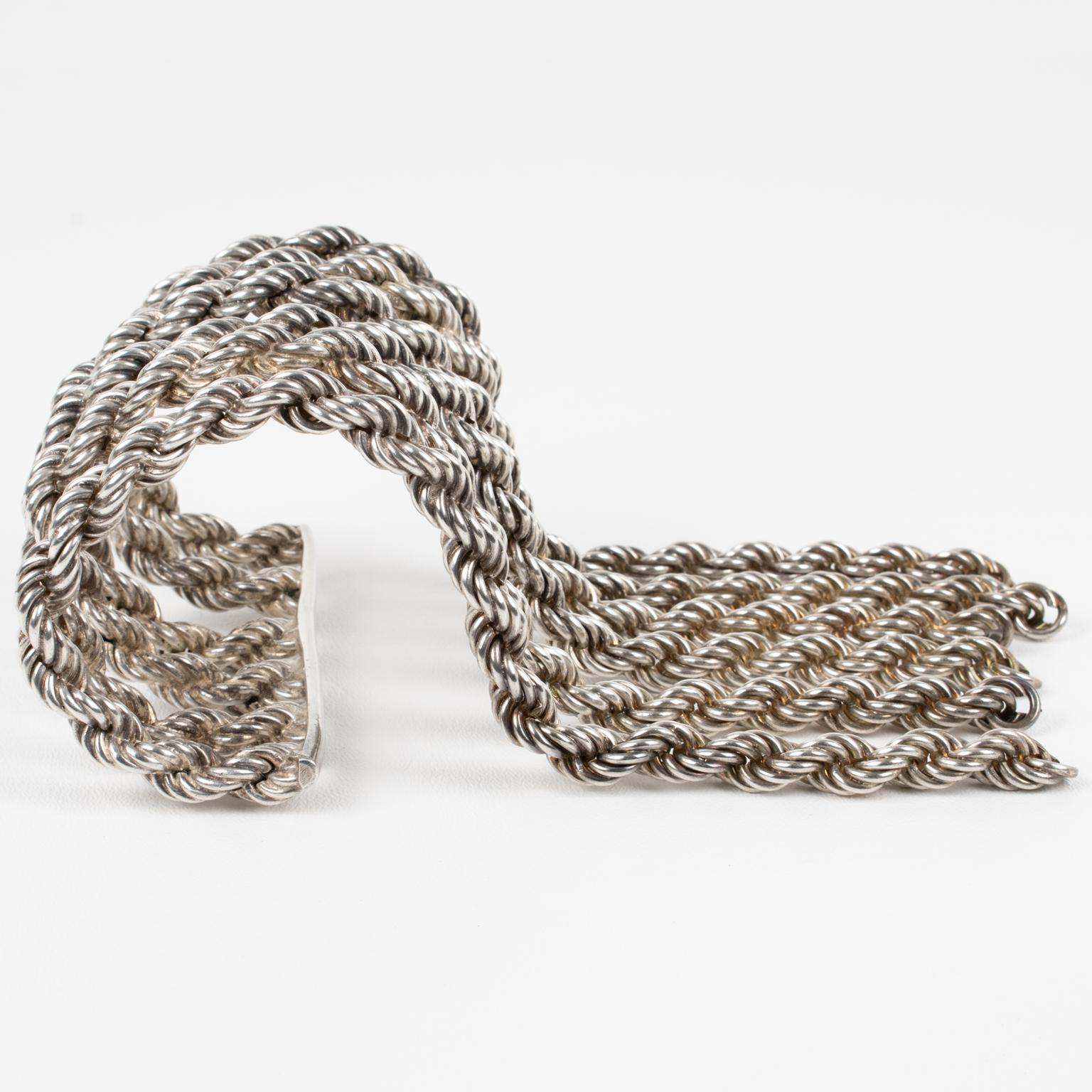 Ce spectaculaire et incroyable bracelet manchette Mercedes Looping Paris est composé d'une manchette en métal argenté avec de lourdes chaînes à boucles et des charmes. 
Les chaînes qui forment ce bracelet sont attachées d'un côté à une barre