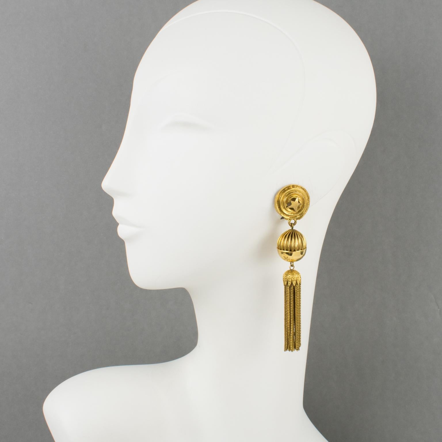 Ultra-chic Mercedes Robirosa Paris clip-on earrings. Oversized dangling baroque style with gilt metal all textured and carved featuring stars carving, striped bead, and long metal tassel. Signed at the back with the brand logo.
Measurements: 4.13