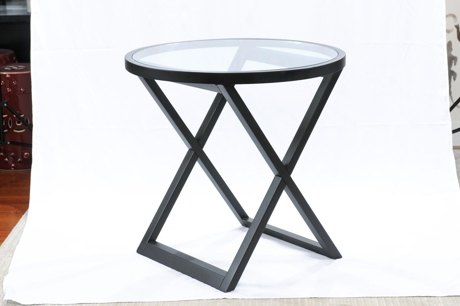 Ralph Lauren Mercer Street side table. A gorgeous round side table. The top wood frame is veneered in Wood painted black, which gives it a rather elegant sensibility. The glass top keeps the attention on the unique X-shaped base. It will make a